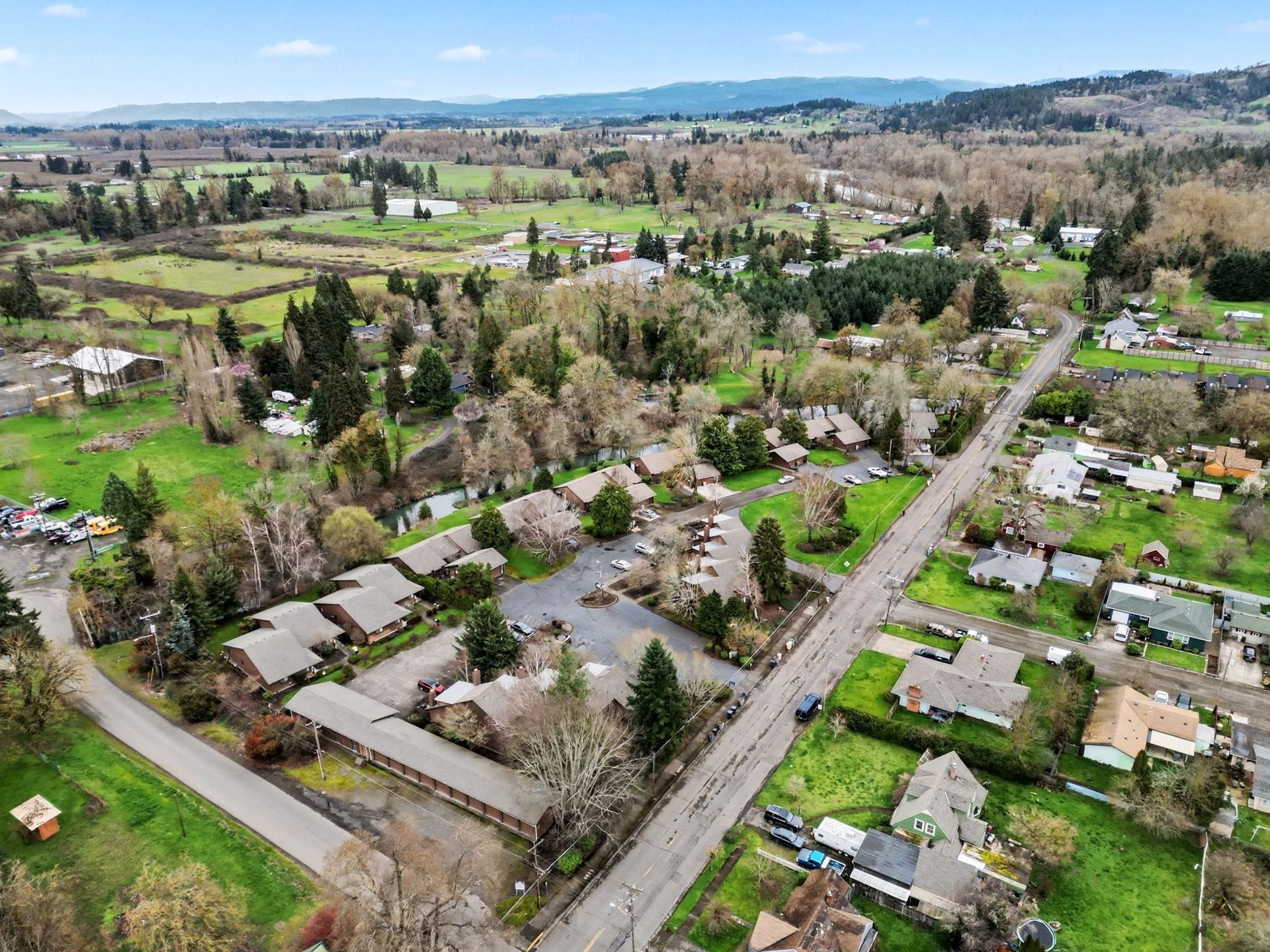 Aerial view of a suburban neighborhood with houses, tree-lined streets, and distant hills under a clear sky