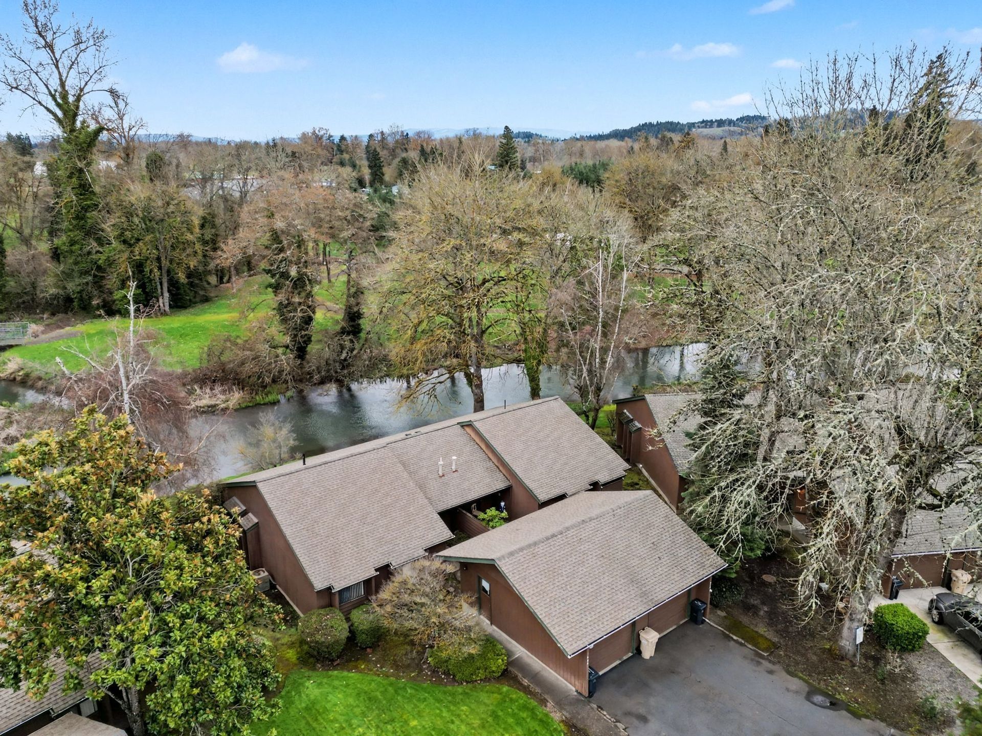 Aerial view of a brown-roofed house beside a pond and trees in a rural landscape.