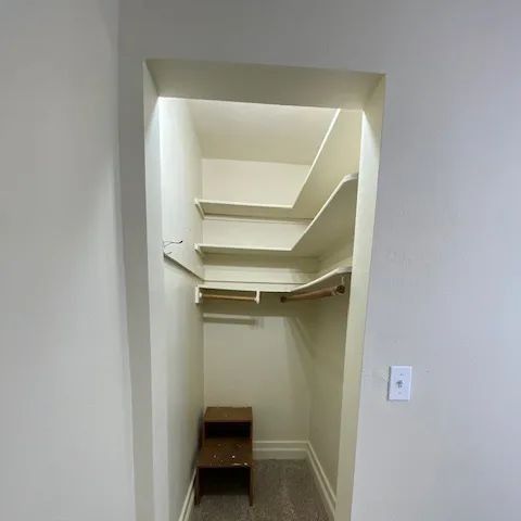 Empty walk-in closet with white walls, built-in shelves, and a small wooden stool.