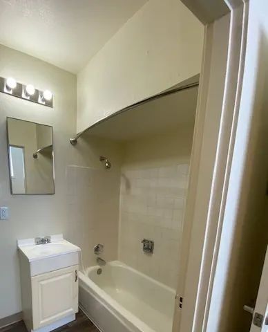 Small bathroom with white tub, vanity, mirror, and light fixture under a sloped ceiling.