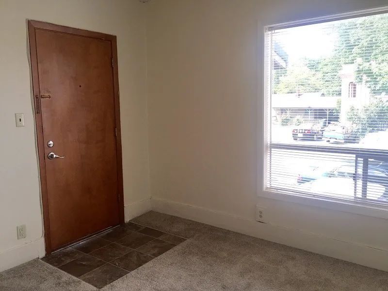 Empty room with brown front door, window, and beige carpet and walls.