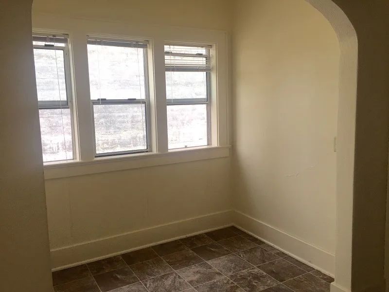 Empty beige room with three windows and a tiled floor
