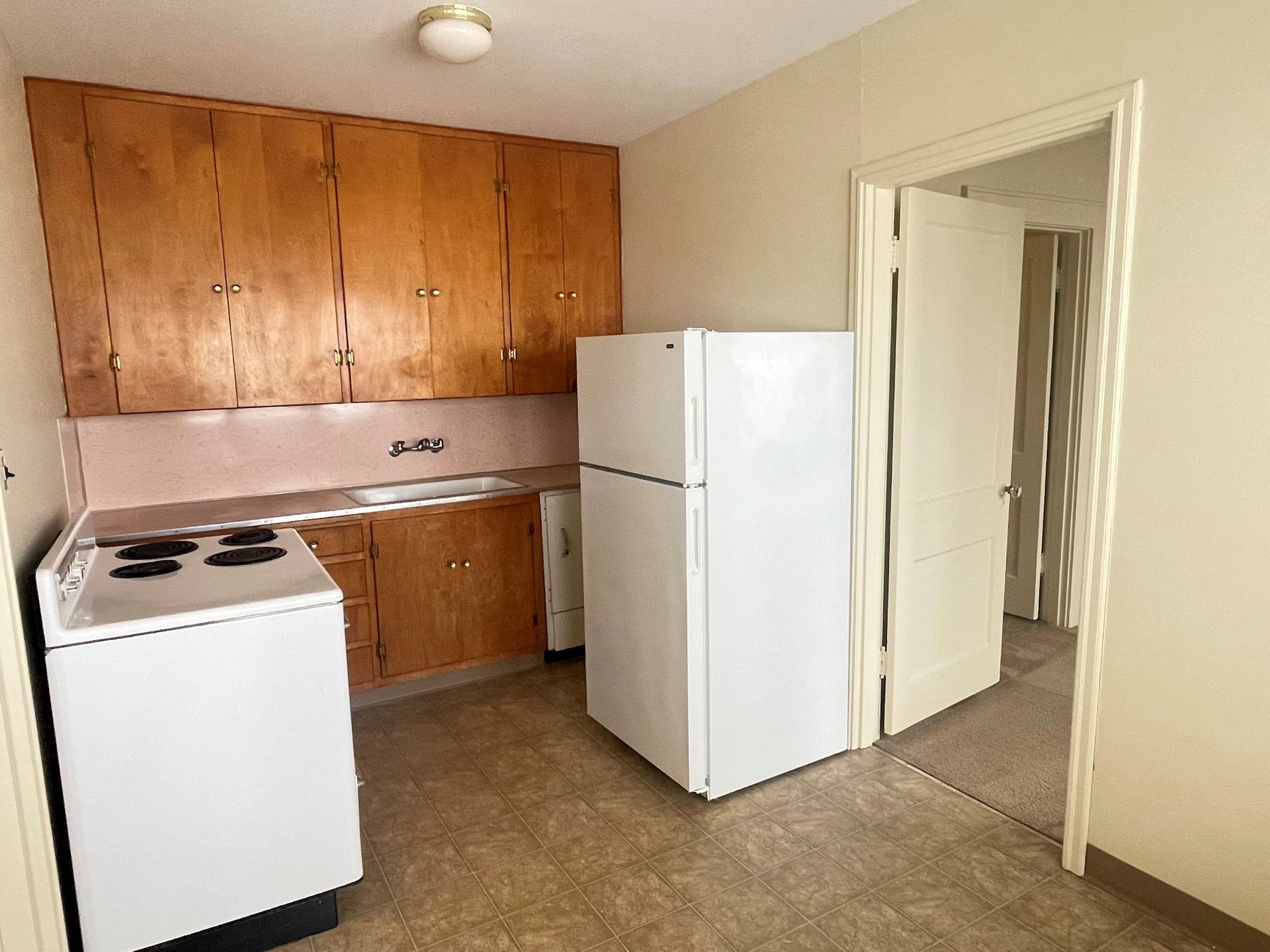 Small kitchen with white appliances, wood cabinets, and an open doorway.