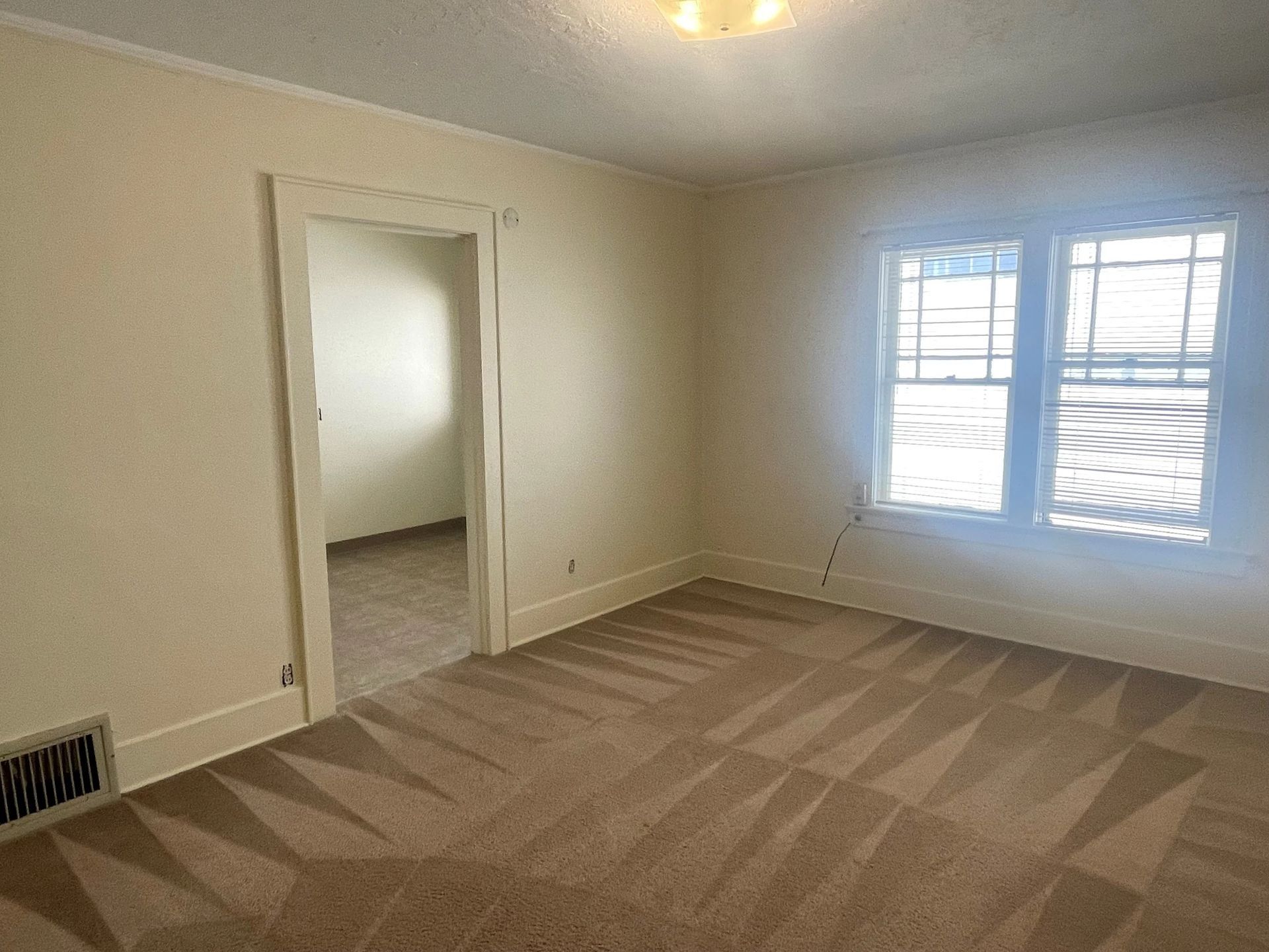 Empty beige bedroom with carpet, open doorway, and window letting in daylight