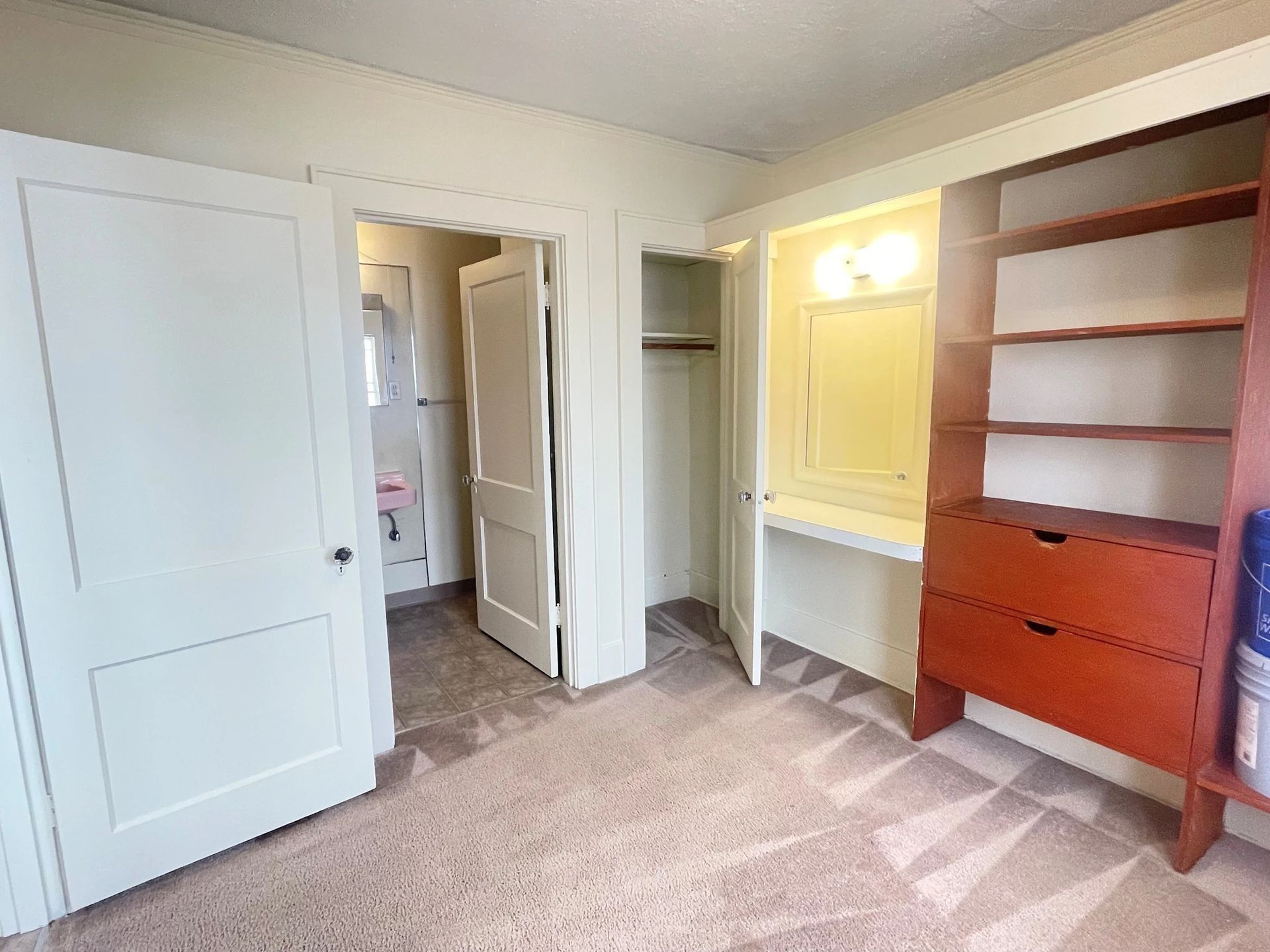 Empty carpeted bedroom with open closet, white doors, and wooden shelving unit