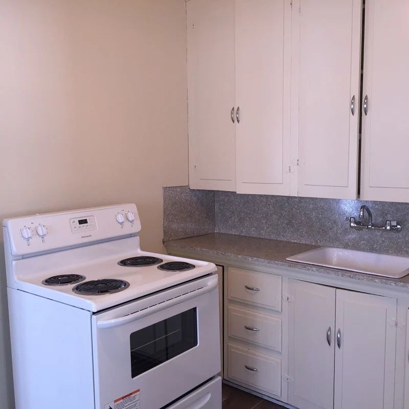 Small beige kitchen with white stove, cabinets, sink, and speckled backsplash.