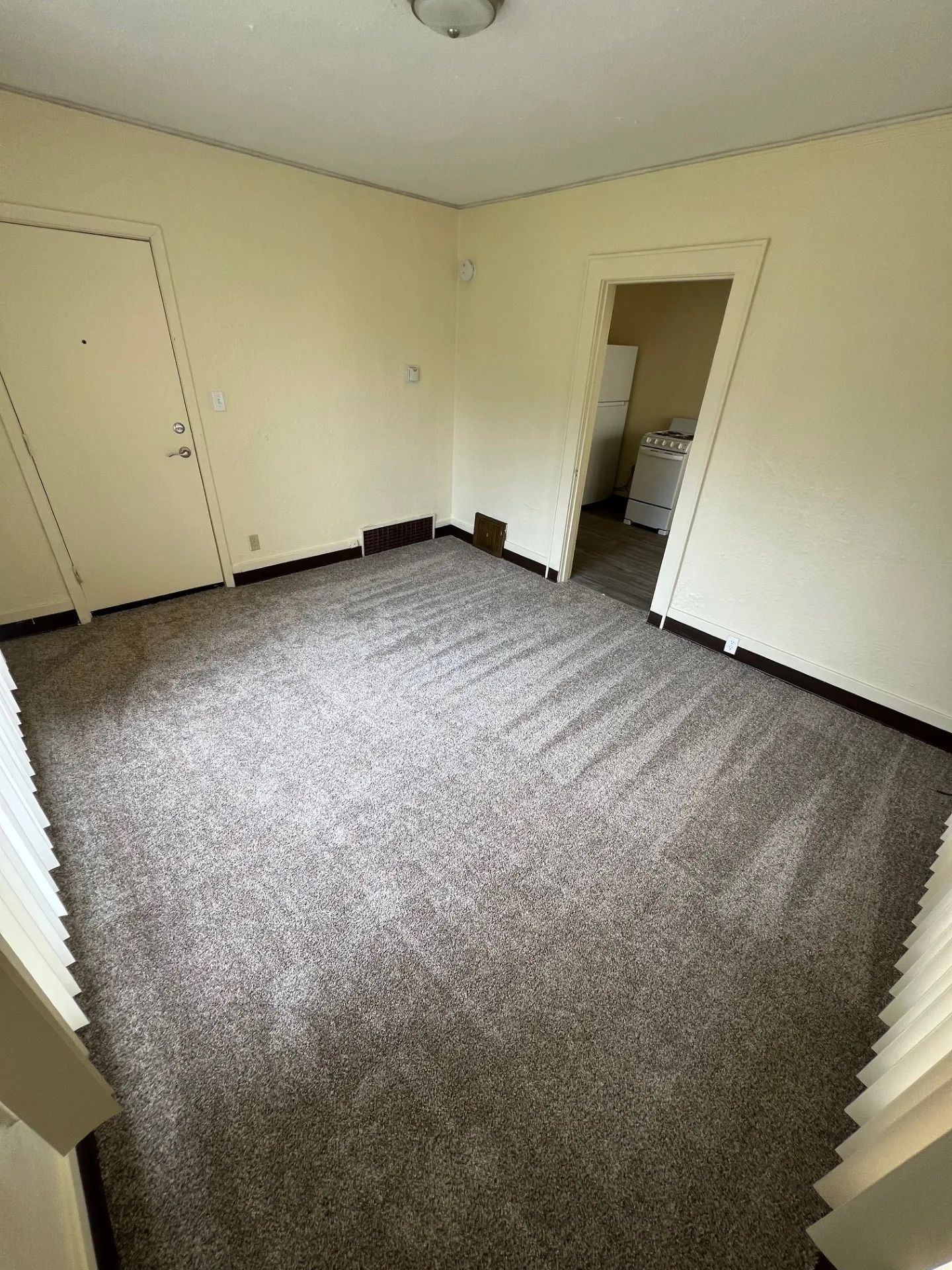 Empty beige bedroom with gray carpet and an open doorway to a bathroom