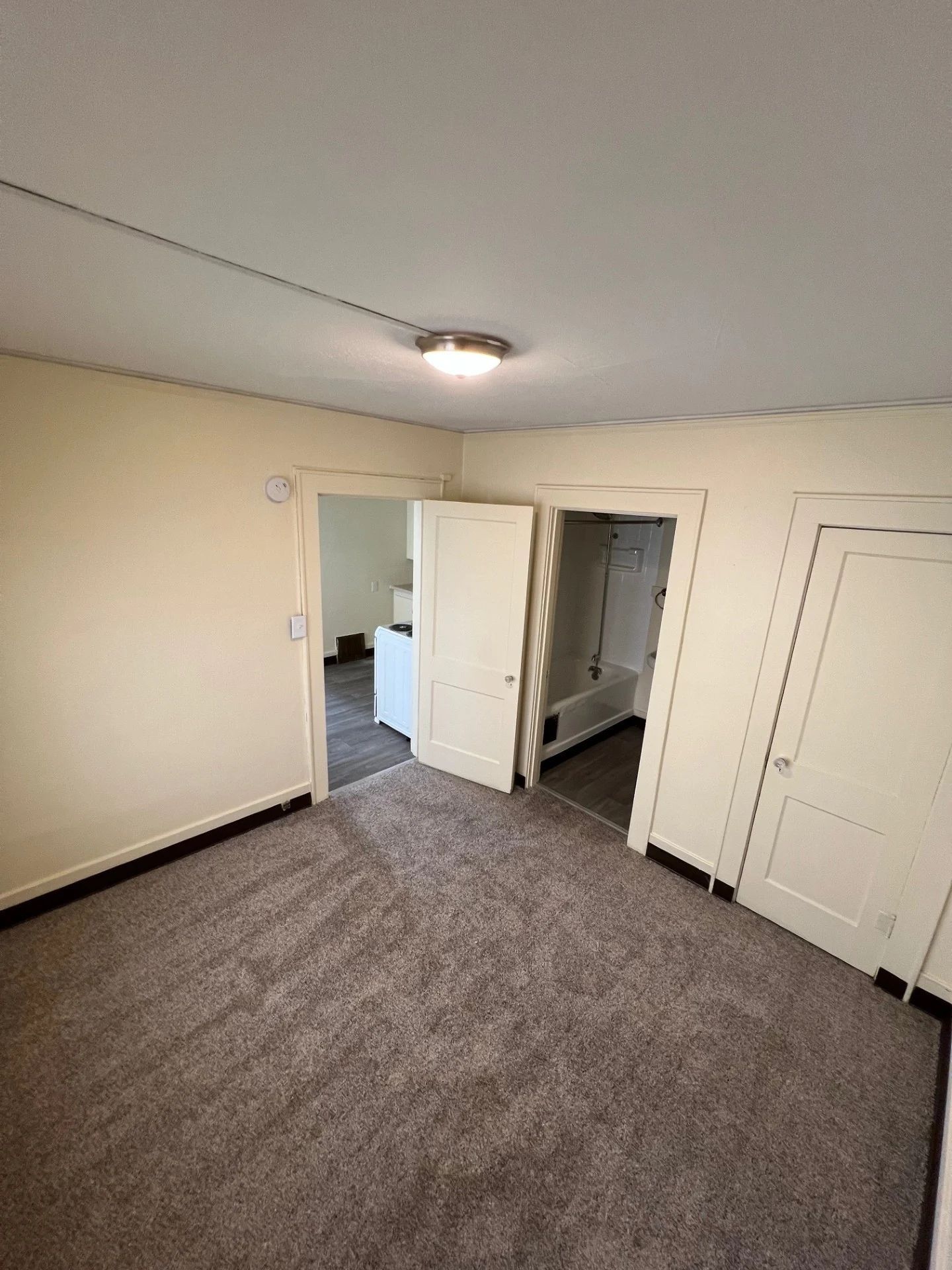Empty beige bedroom with carpet, white doors, and a doorway to a bathroom or closet.
