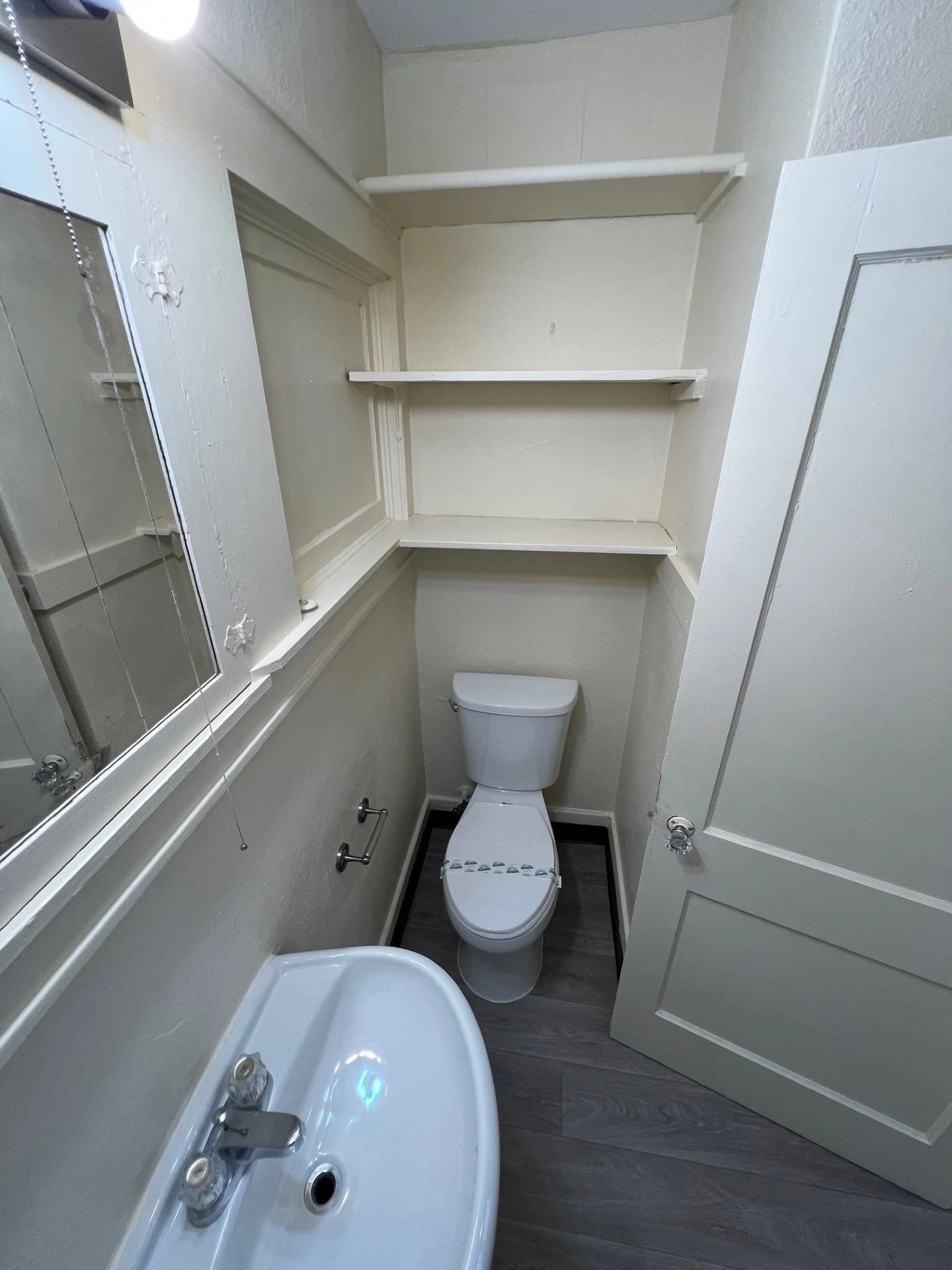 Small bathroom with toilet, sink, mirror, and built-in shelves in a narrow alcove.