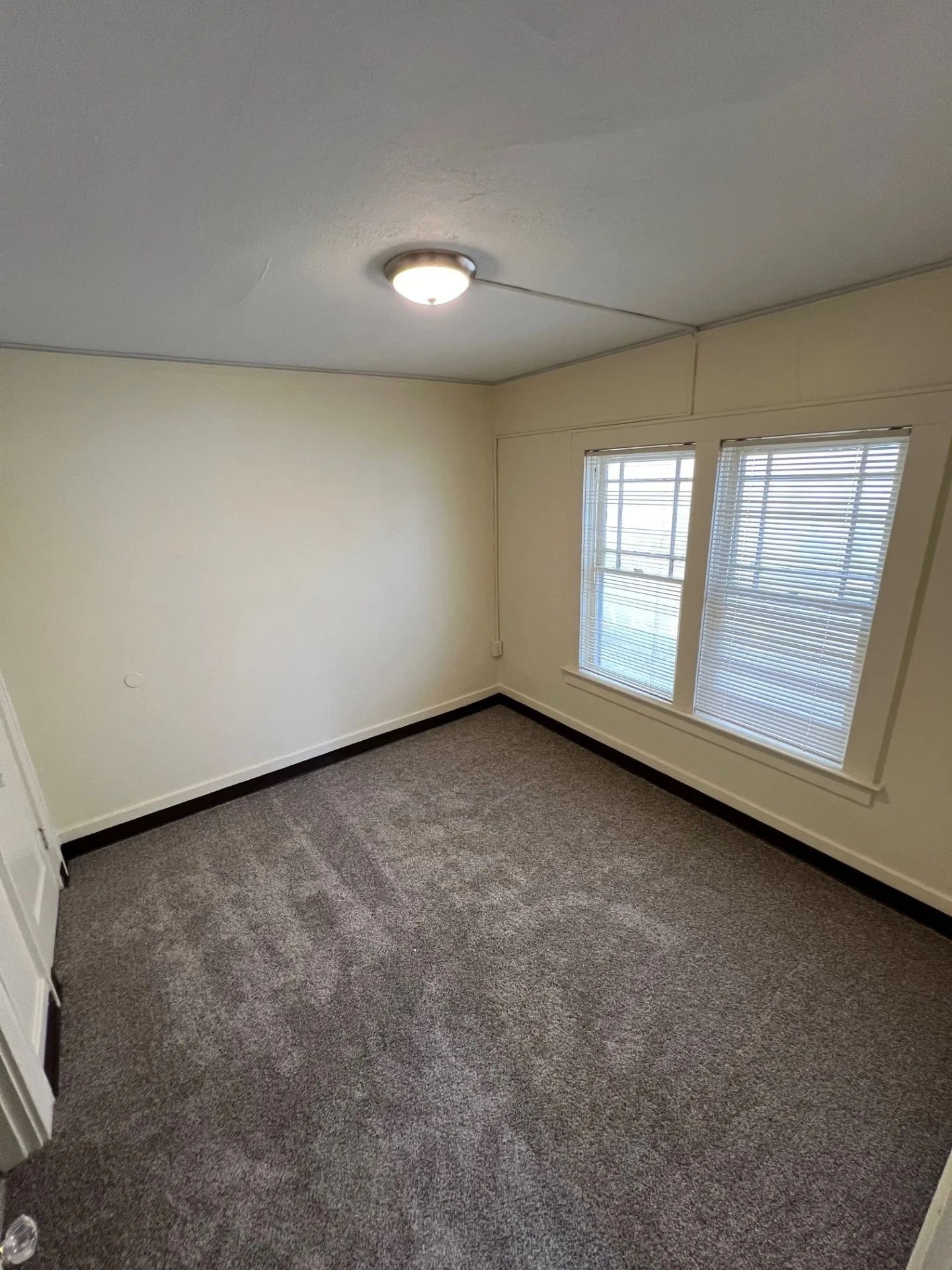 Empty beige room with gray carpet and two windows with white blinds