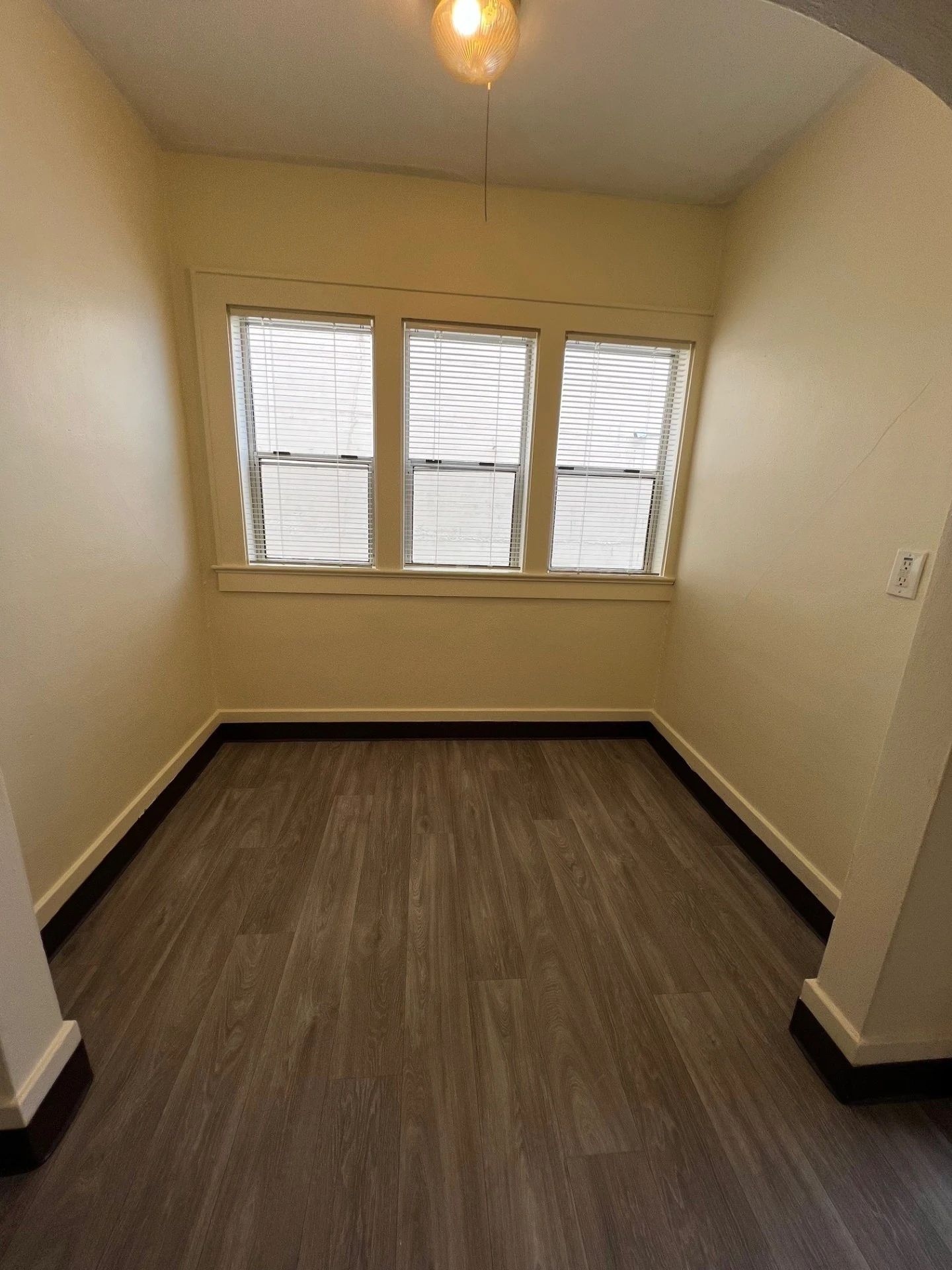 Small empty room with beige walls, dark wood floor, and a three-pane window.