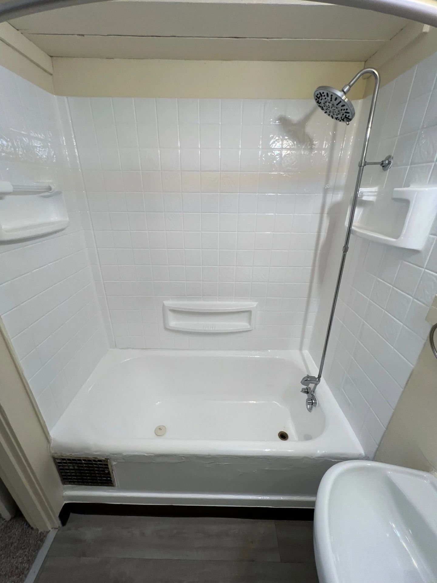 White tiled bathtub and shower stall with grab bars, built-in shelves, and showerhead.