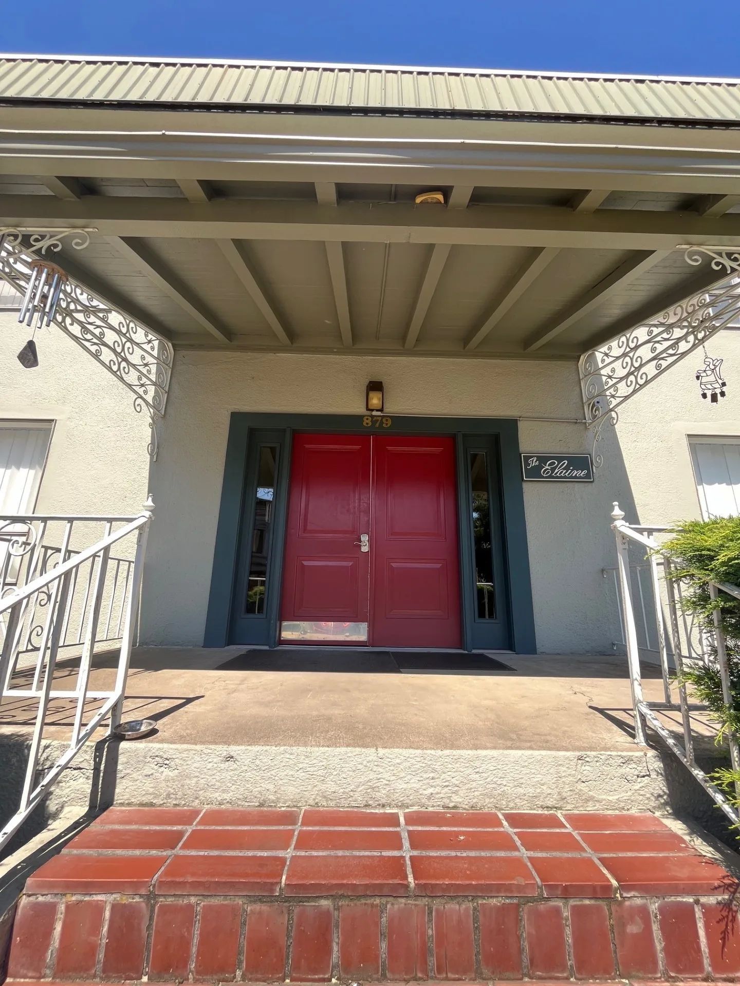 Front entrance with red double doors, brick steps, and a covered porch with railings