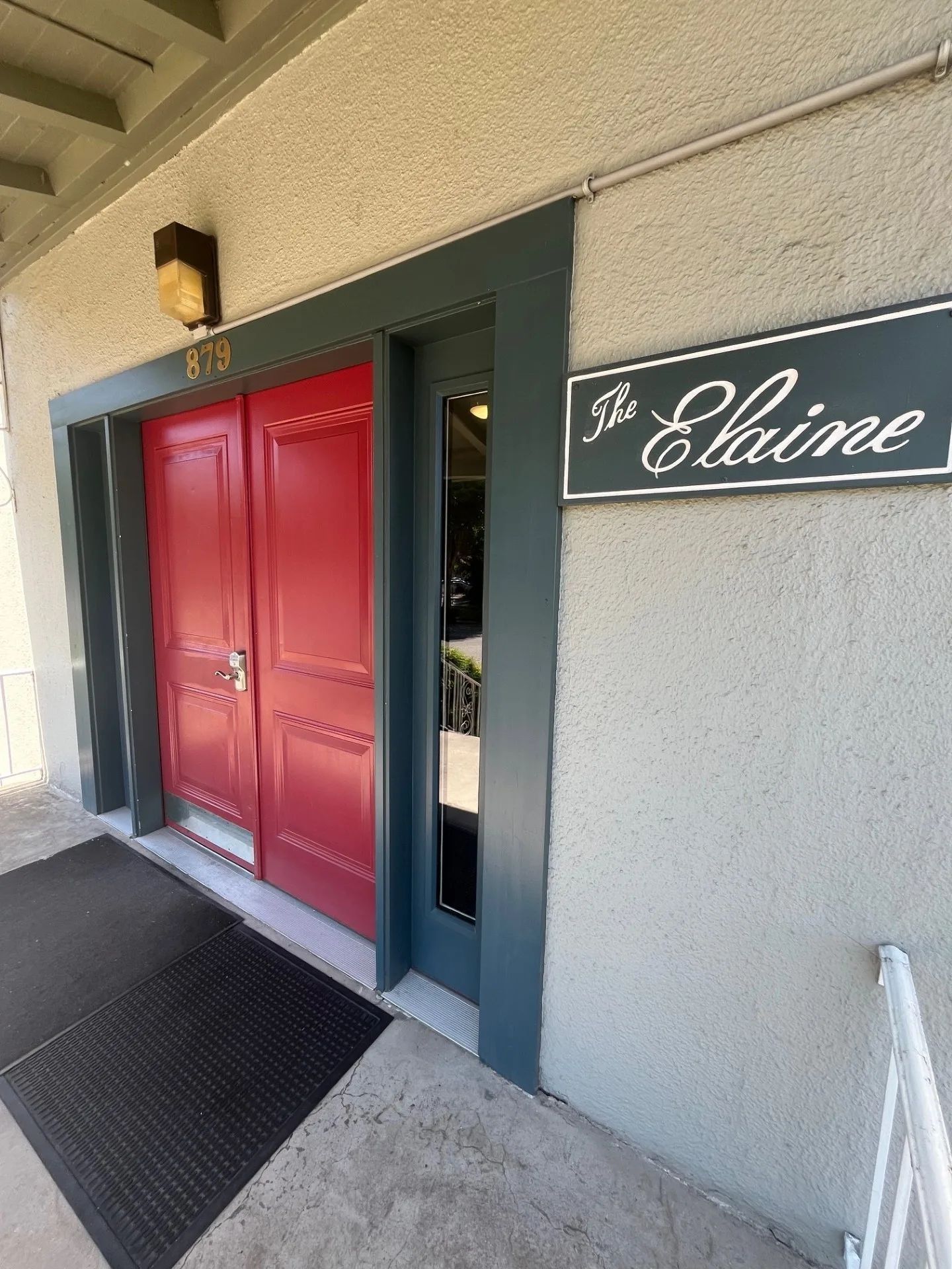 Red double doors beside a gray wall with a sign reading “Elaine” above the entrance.