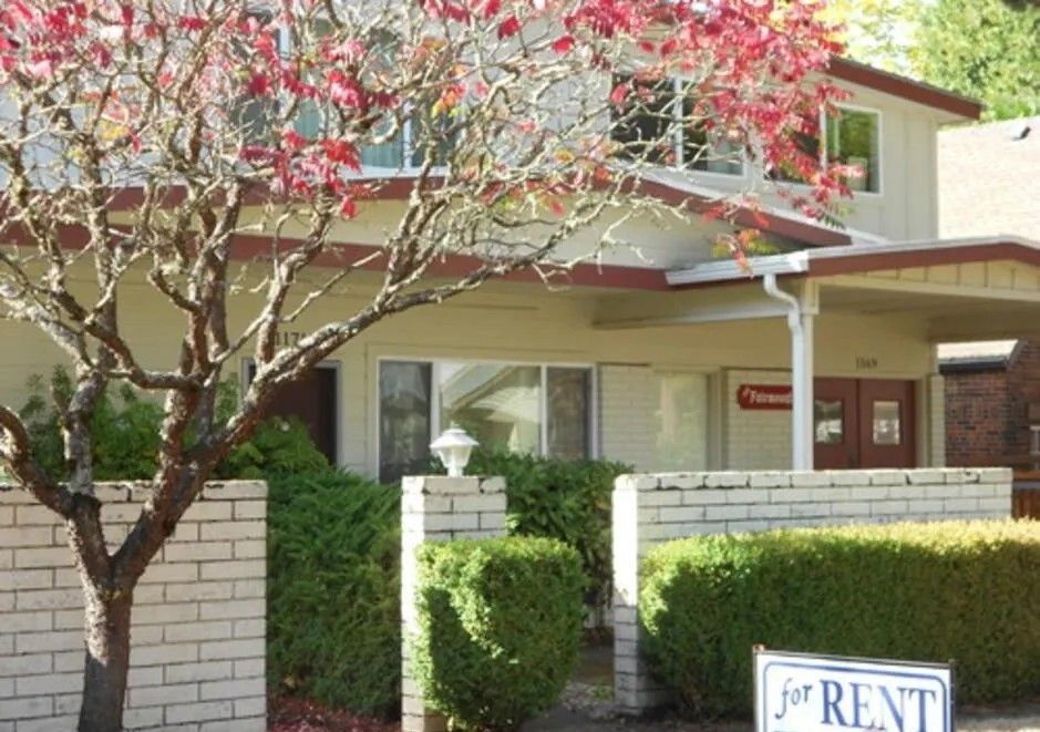 Apartment building with a for rent sign and flowering tree in front