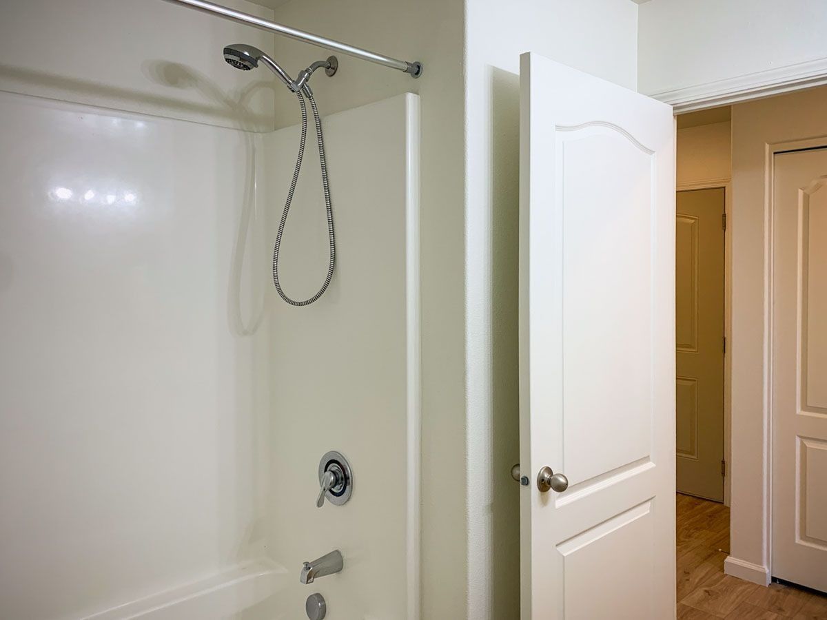 White bathroom shower with chrome fixtures, open door, and hallway visible outside