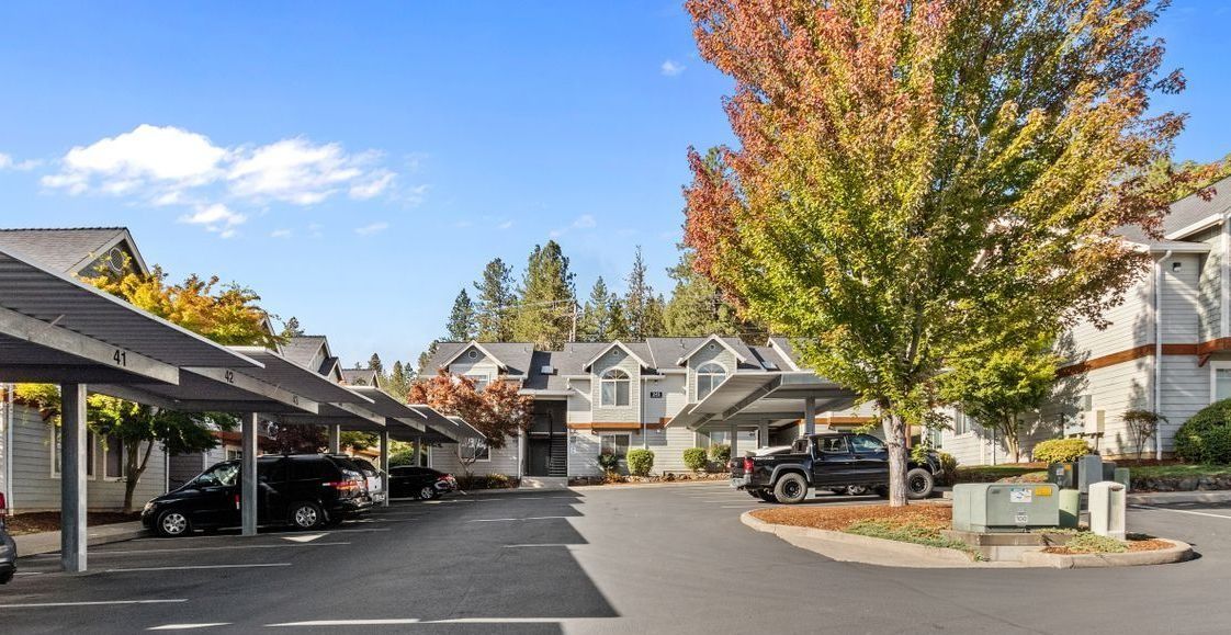 Apartment complex parking lot with covered spaces, autumn trees, and parked cars under a clear blue sky
