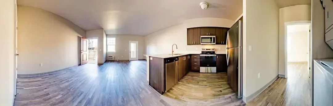 Empty open-plan apartment with wood floors, kitchen island, and large windows overlooking a city view