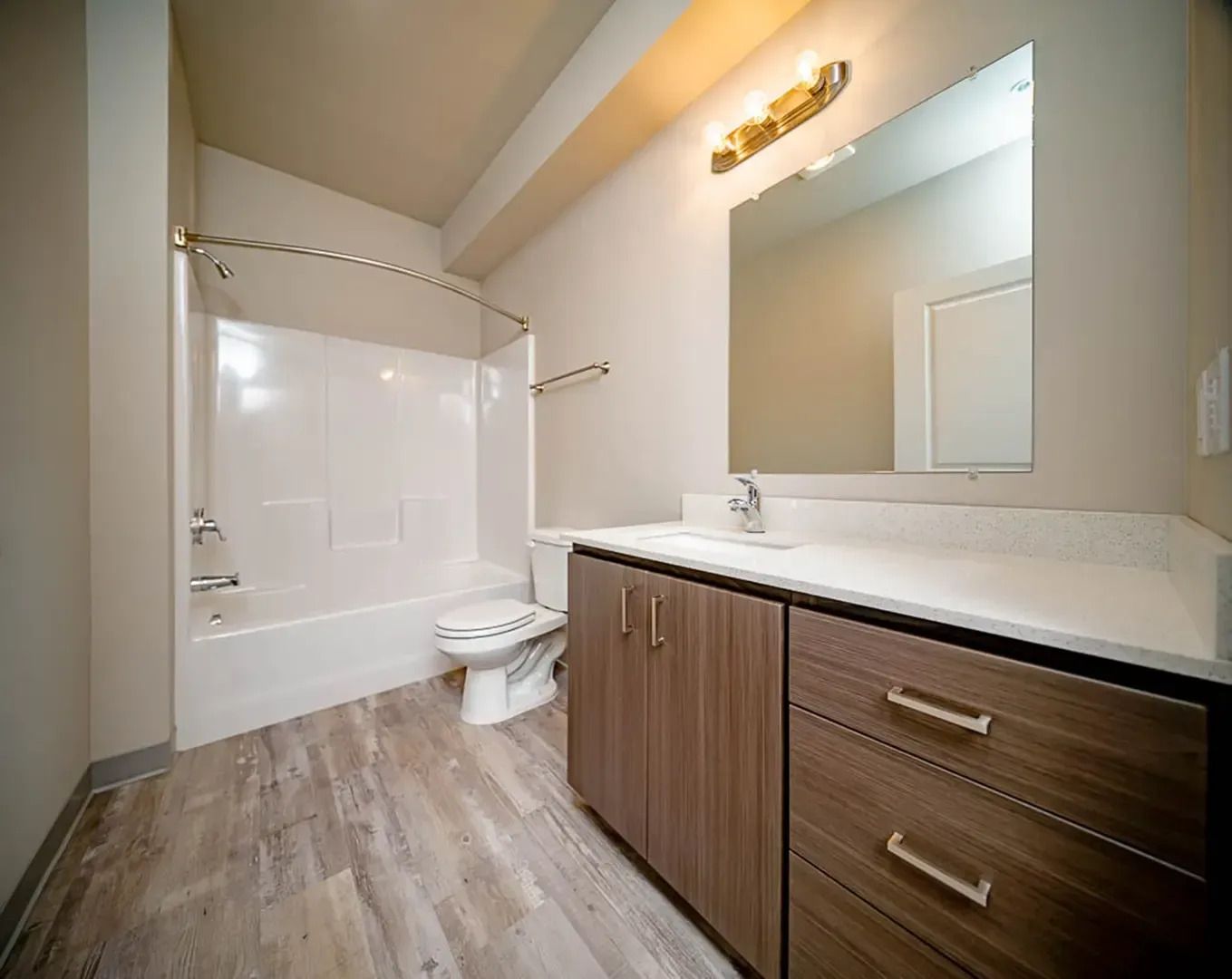 Modern bathroom with wood vanity, large mirror, toilet, and white bathtub-shower combo