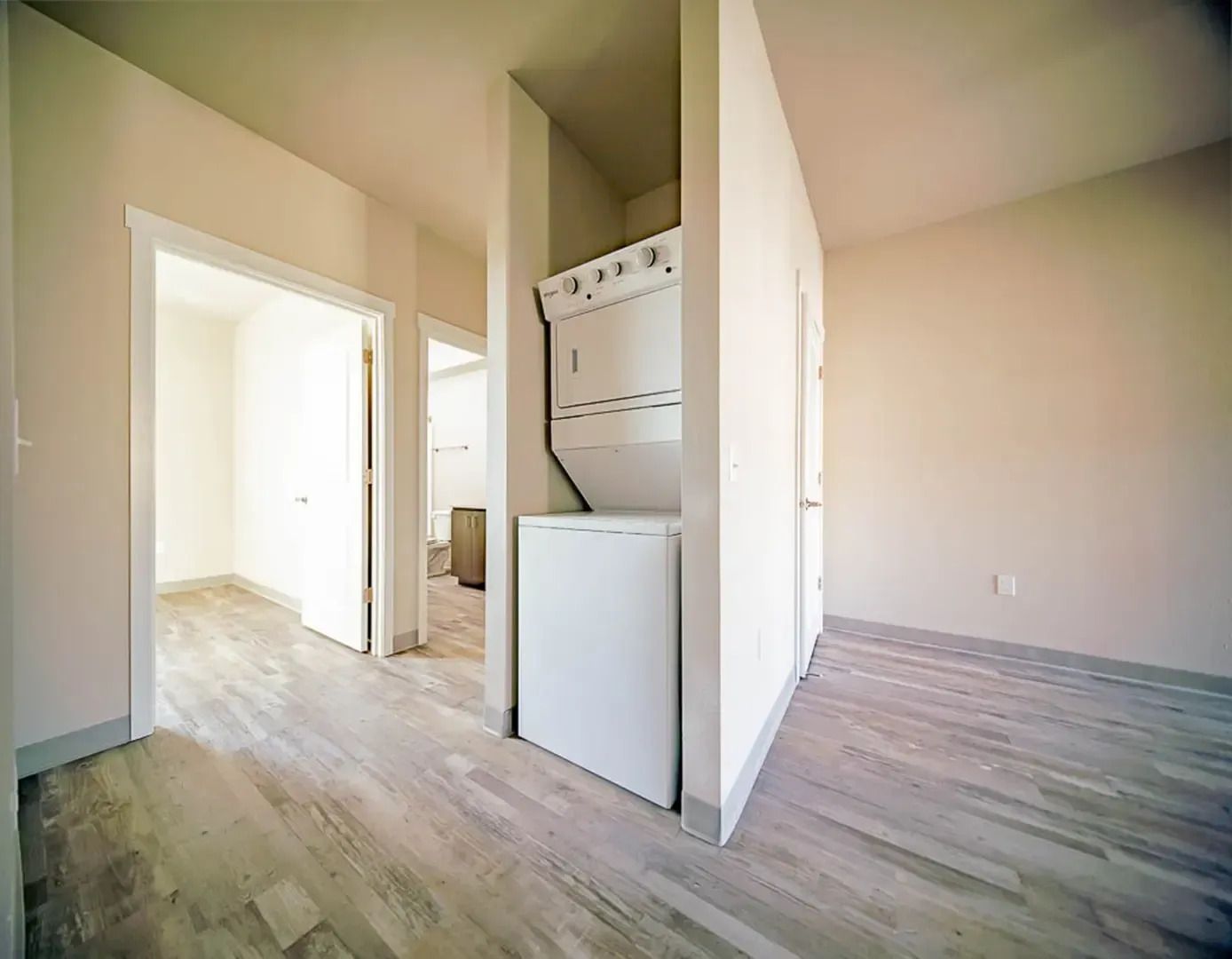 Empty apartment entryway with light wood floors and a laundry nook in the hallway