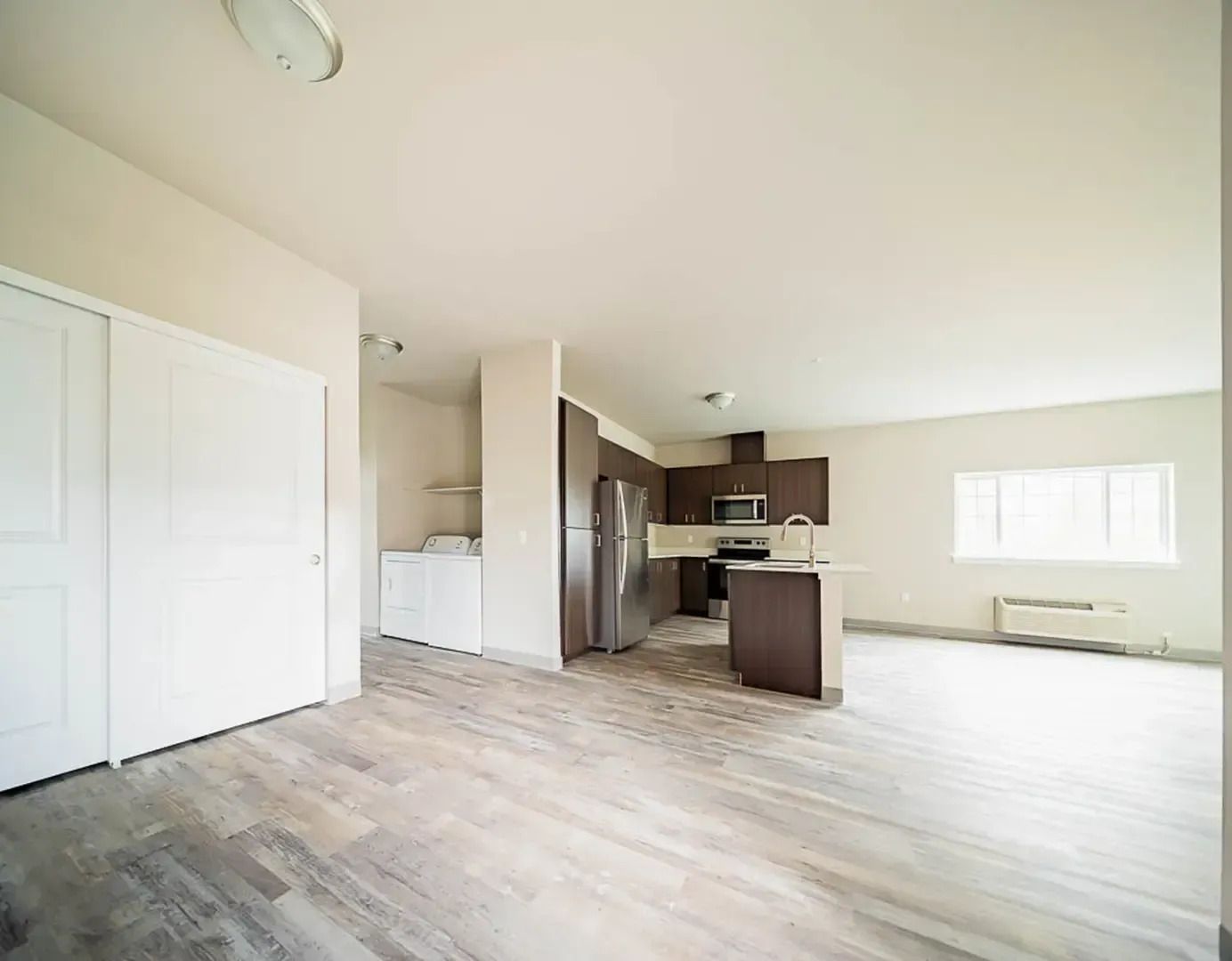 Bright empty open-plan living room with kitchen island, white walls, and large windows