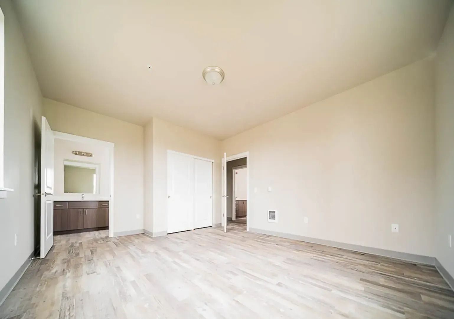 Empty beige apartment living room with wood floors and adjacent kitchen area