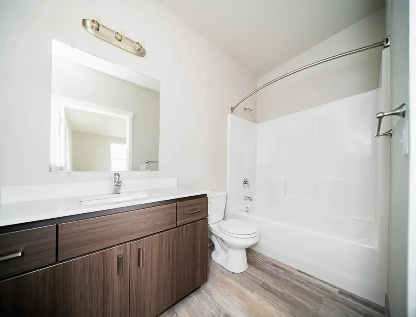 Modern bathroom with dark wood vanity, large mirror, white tub-shower, and light wood flooring