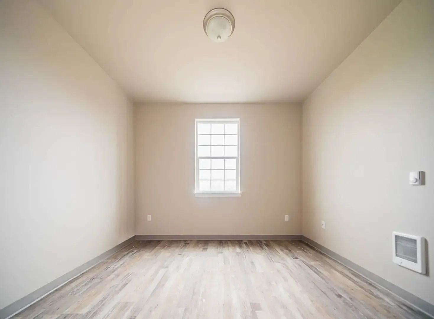 Empty beige room with one window, wood-look floor, and ceiling light