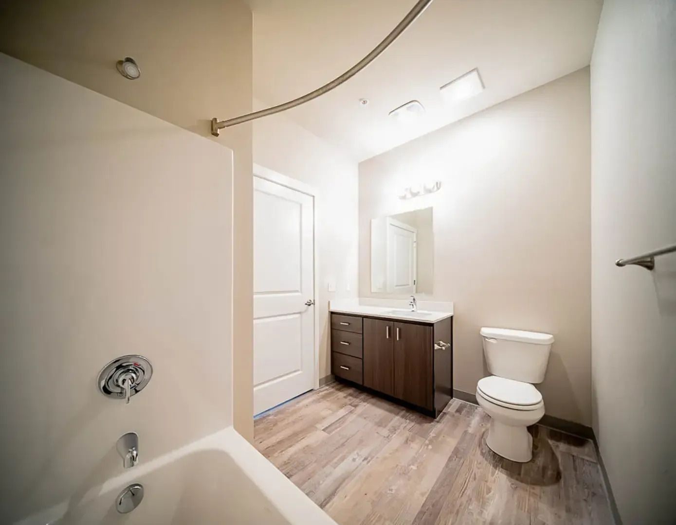 Bright white bathroom with tub, toilet, vanity, mirror, and wood-look floor