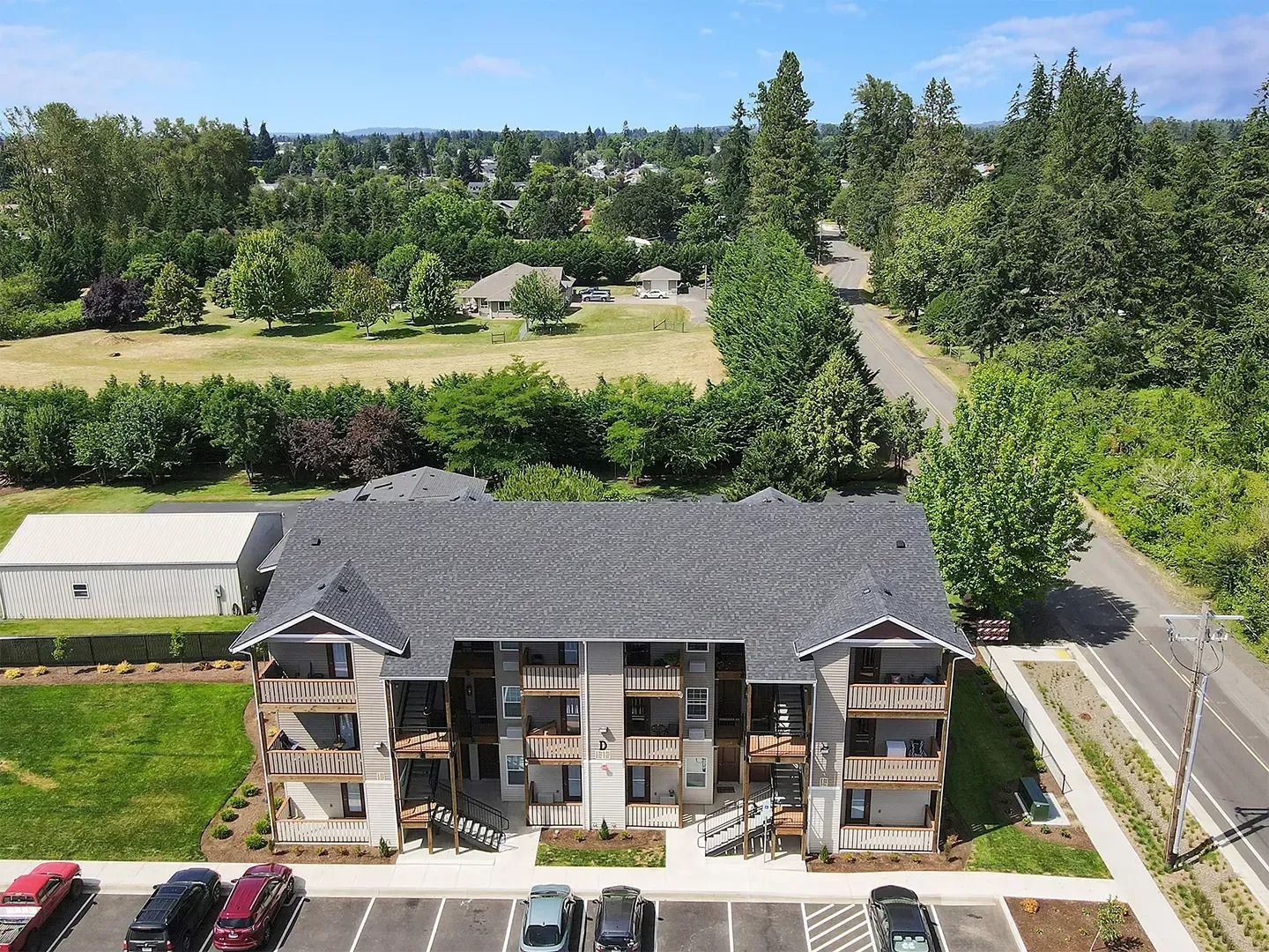 Aerial view of a gray-roofed apartment building beside a road and green trees.