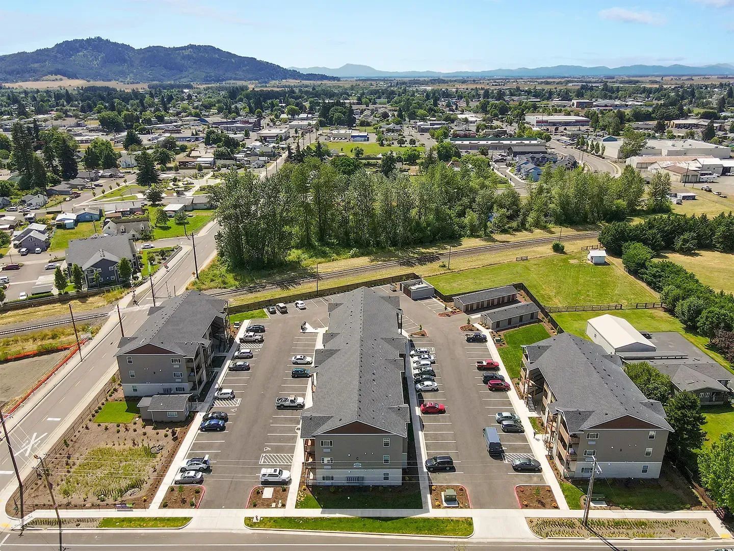 Aerial view of apartment complex with parking lots, trees, and a townscape in the distance.