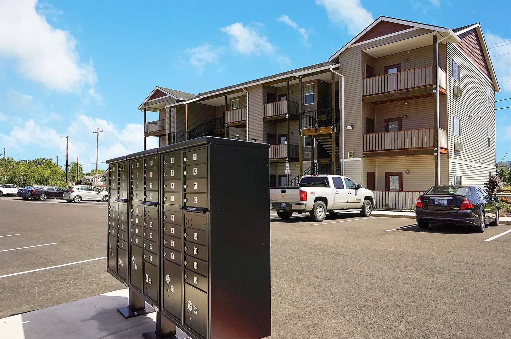 Apartment parking lot with mailboxes in front of a three-story building and parked cars