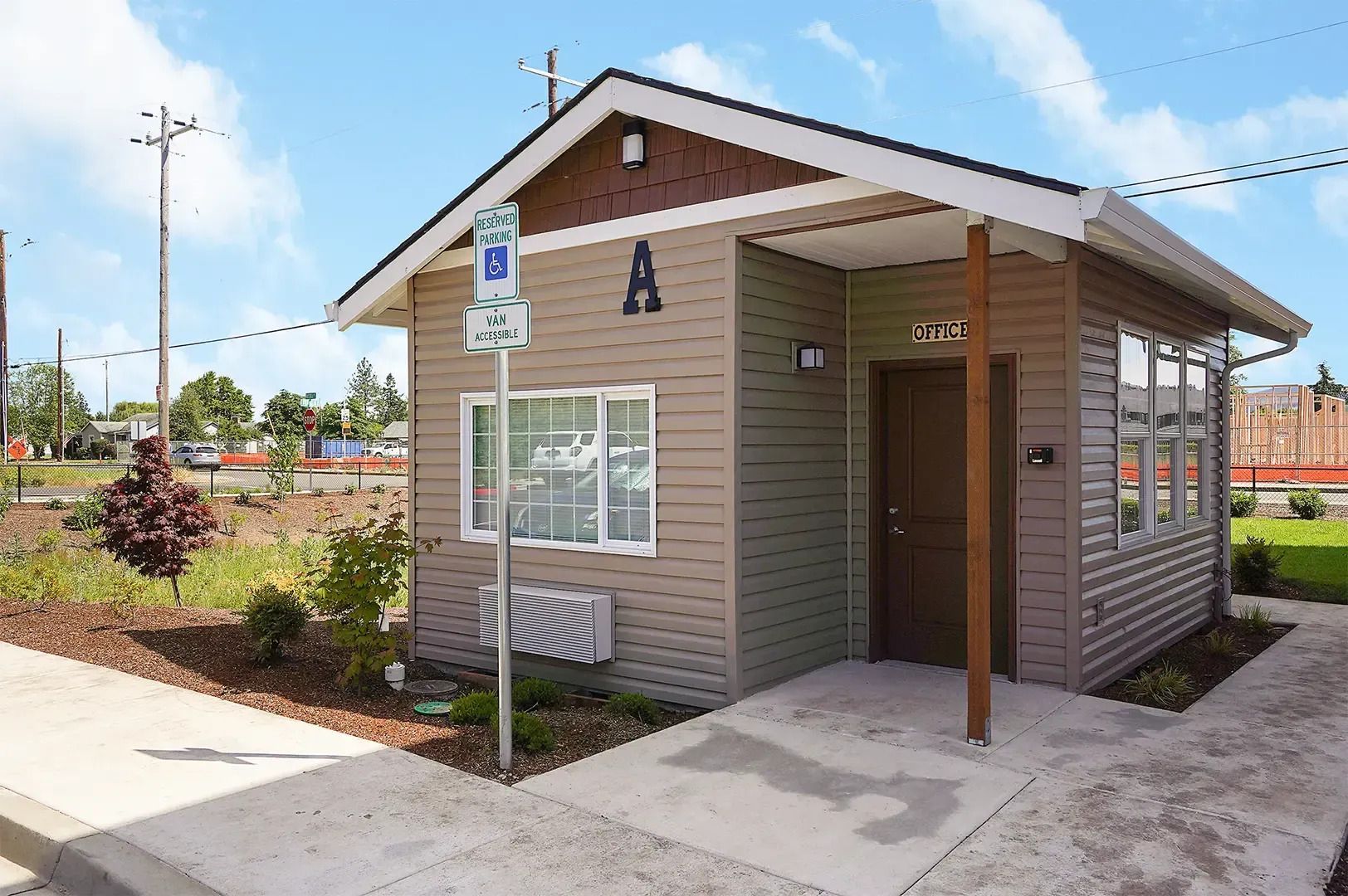 Small tan guardhouse with an accessible ramp, set beside a sidewalk and landscaped area under a blue sky