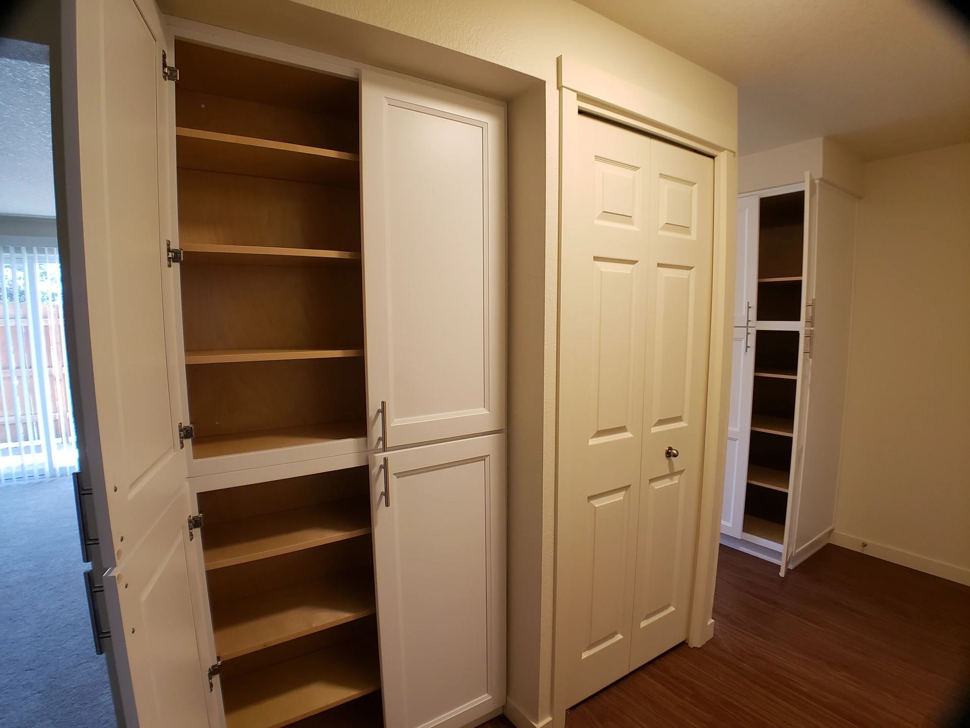 Open closet with wooden shelves beside closed white bedroom closet doors in a beige room