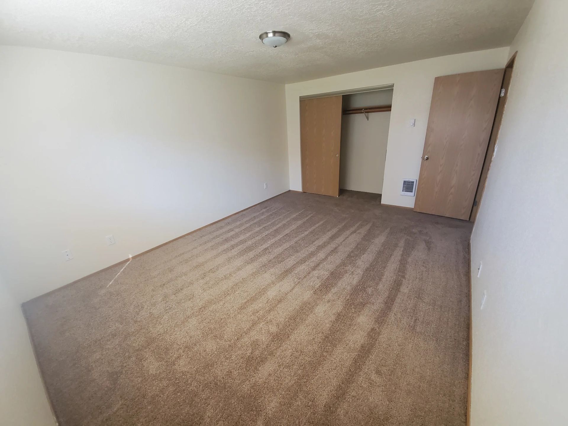 Empty beige-carpeted bedroom with white walls, closet, and open door.