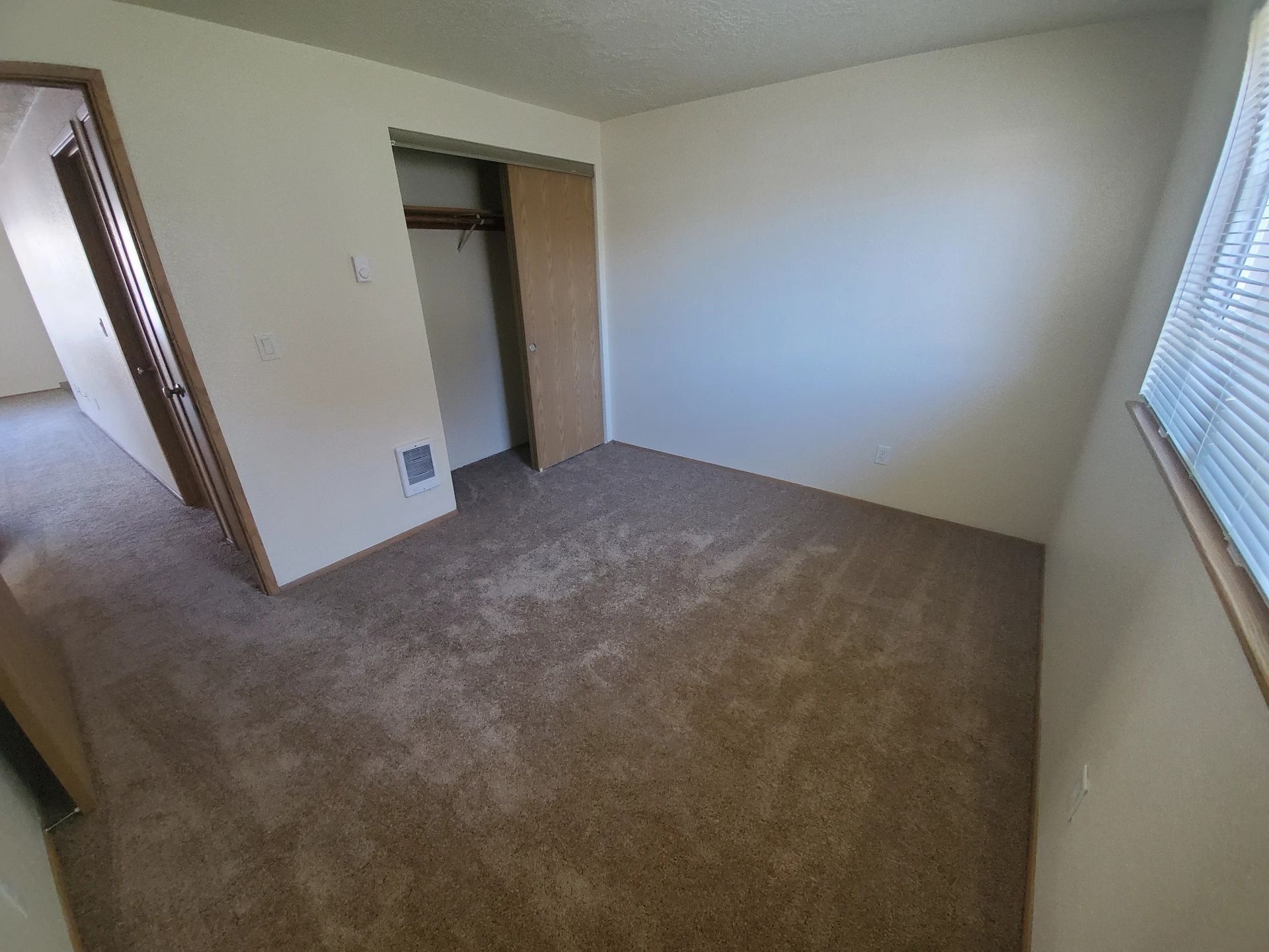 Empty beige bedroom with carpet, closet, and window blinds