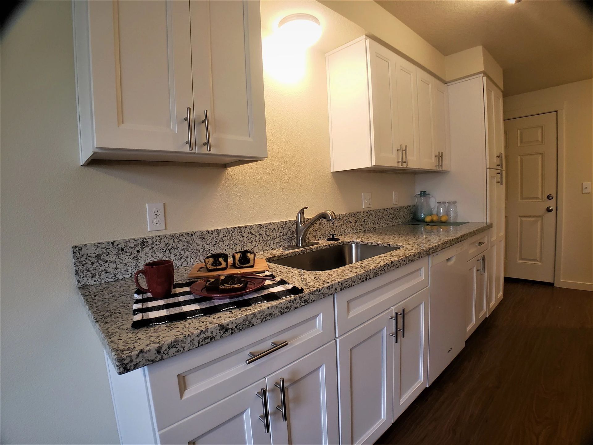 Bright kitchen with white cabinets, speckled granite countertops, and a stove under warm lighting