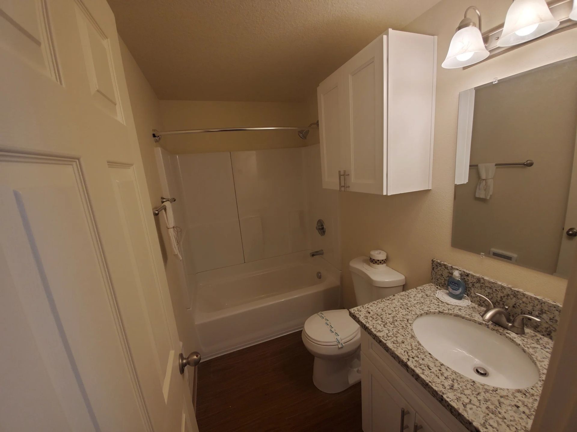 Small bathroom with tub-shower, toilet, sink vanity, mirror, and overhead lights.