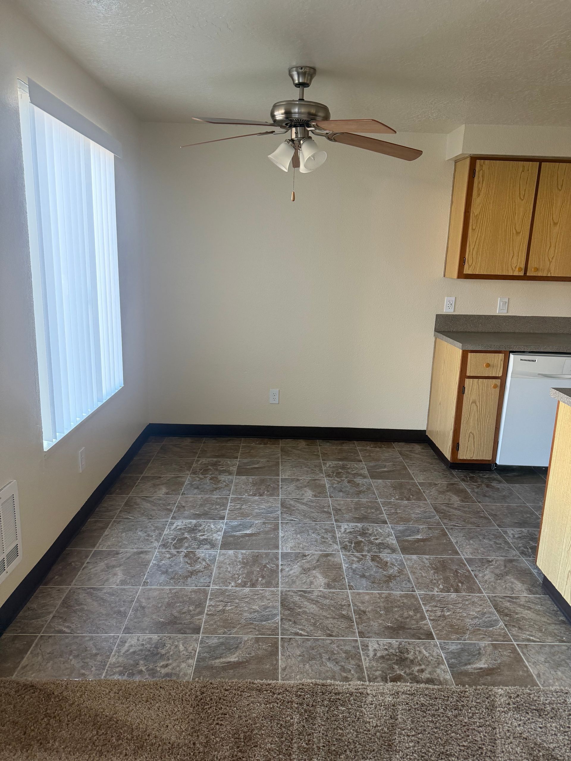 Empty kitchen or dining area with tiled floor, ceiling fan, and window light.
