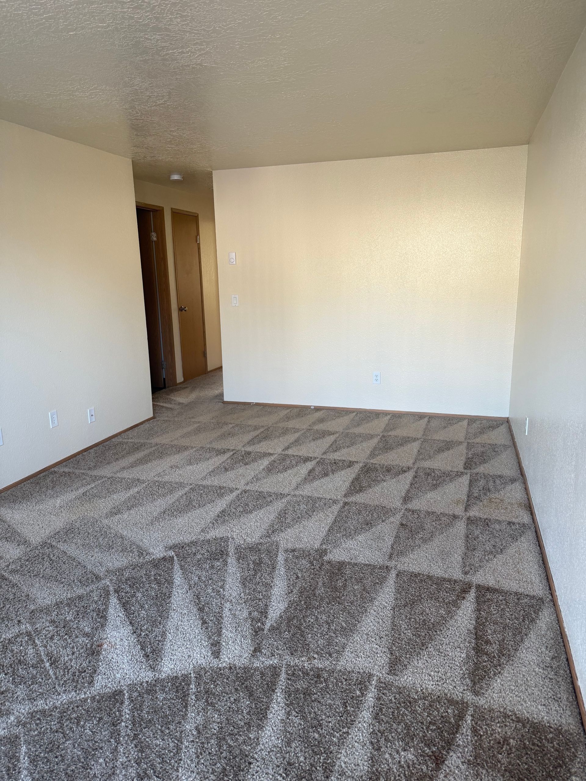 Empty carpeted room with beige walls and an open doorway