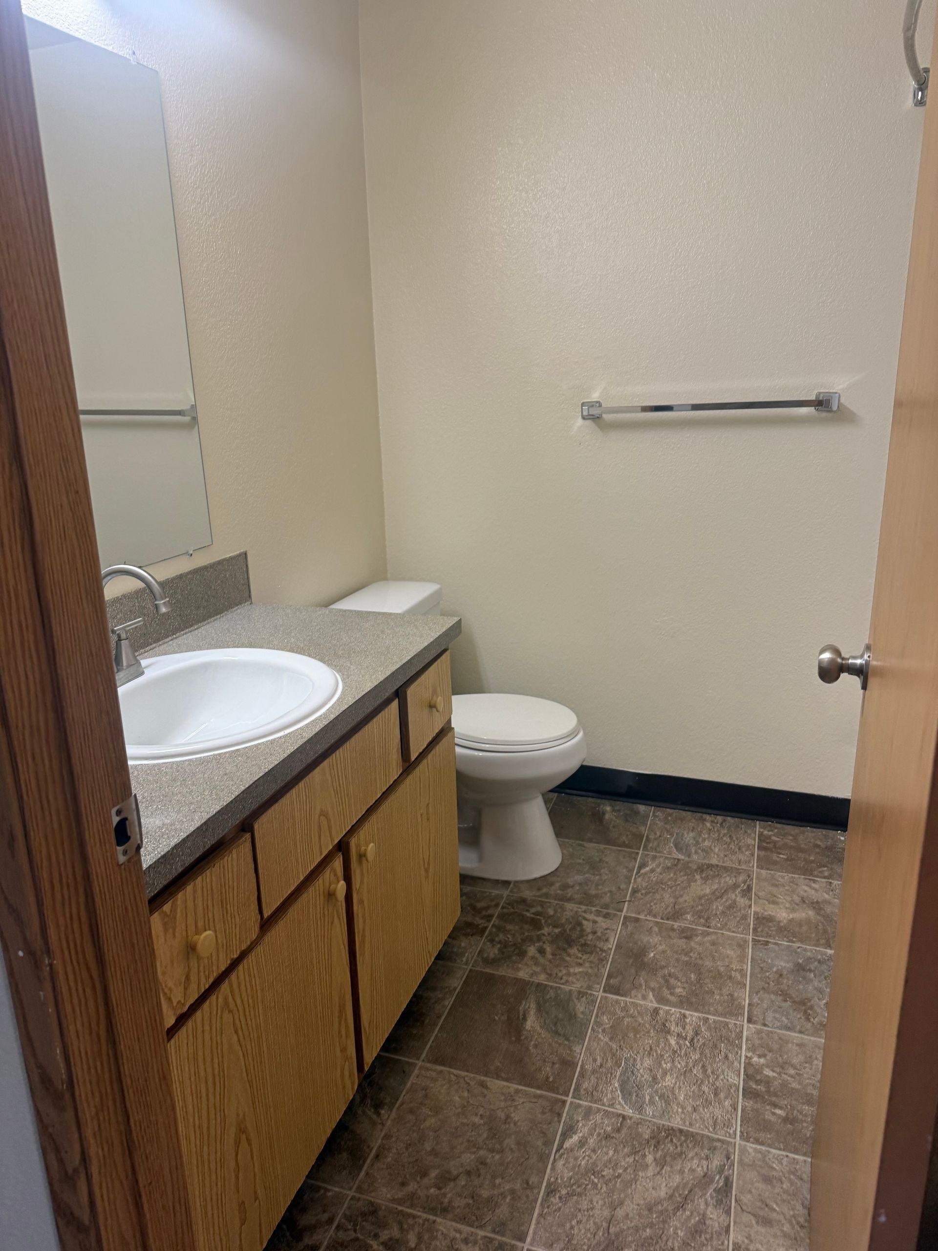 Small bathroom with sink vanity, toilet, towel bar, and tiled floor.