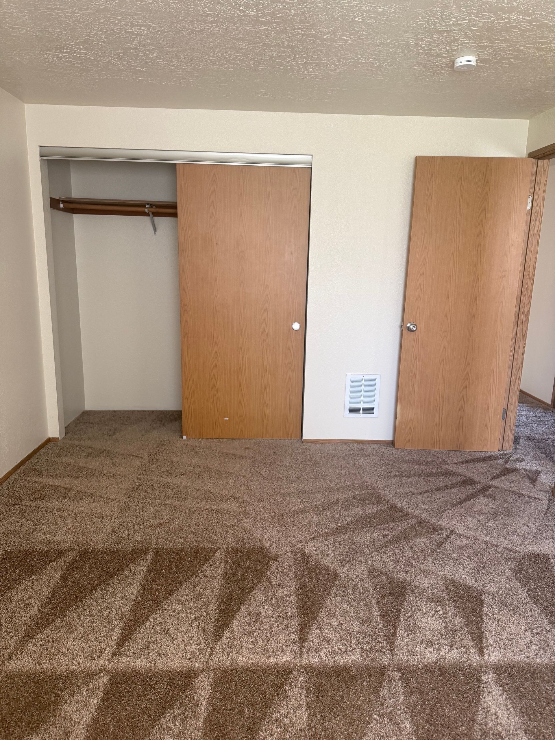 Empty bedroom with open closet doors, brown carpet, and beige walls