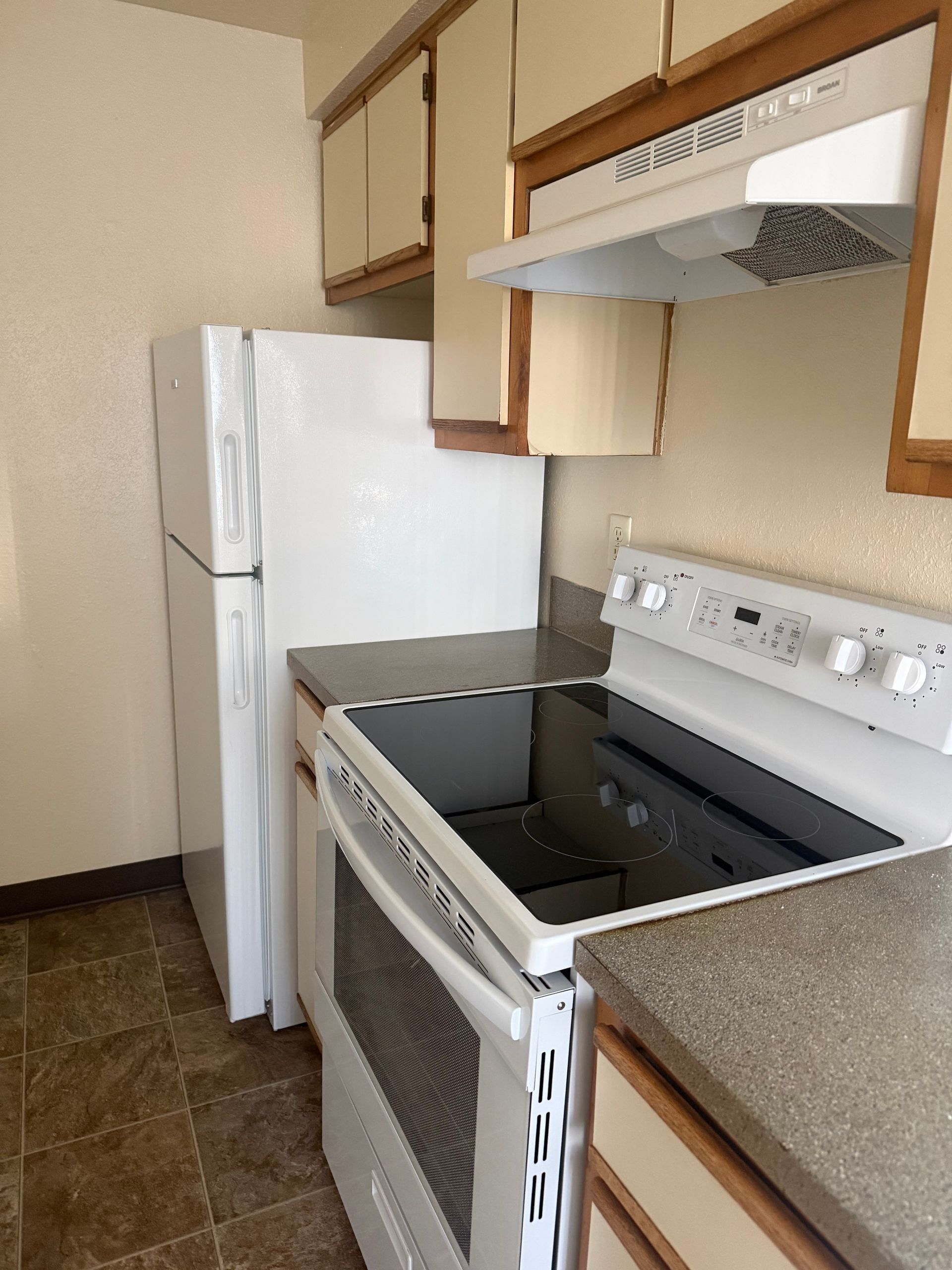 Small kitchen with white appliances, tan cabinets, and a black stove beside a white refrigerator.
