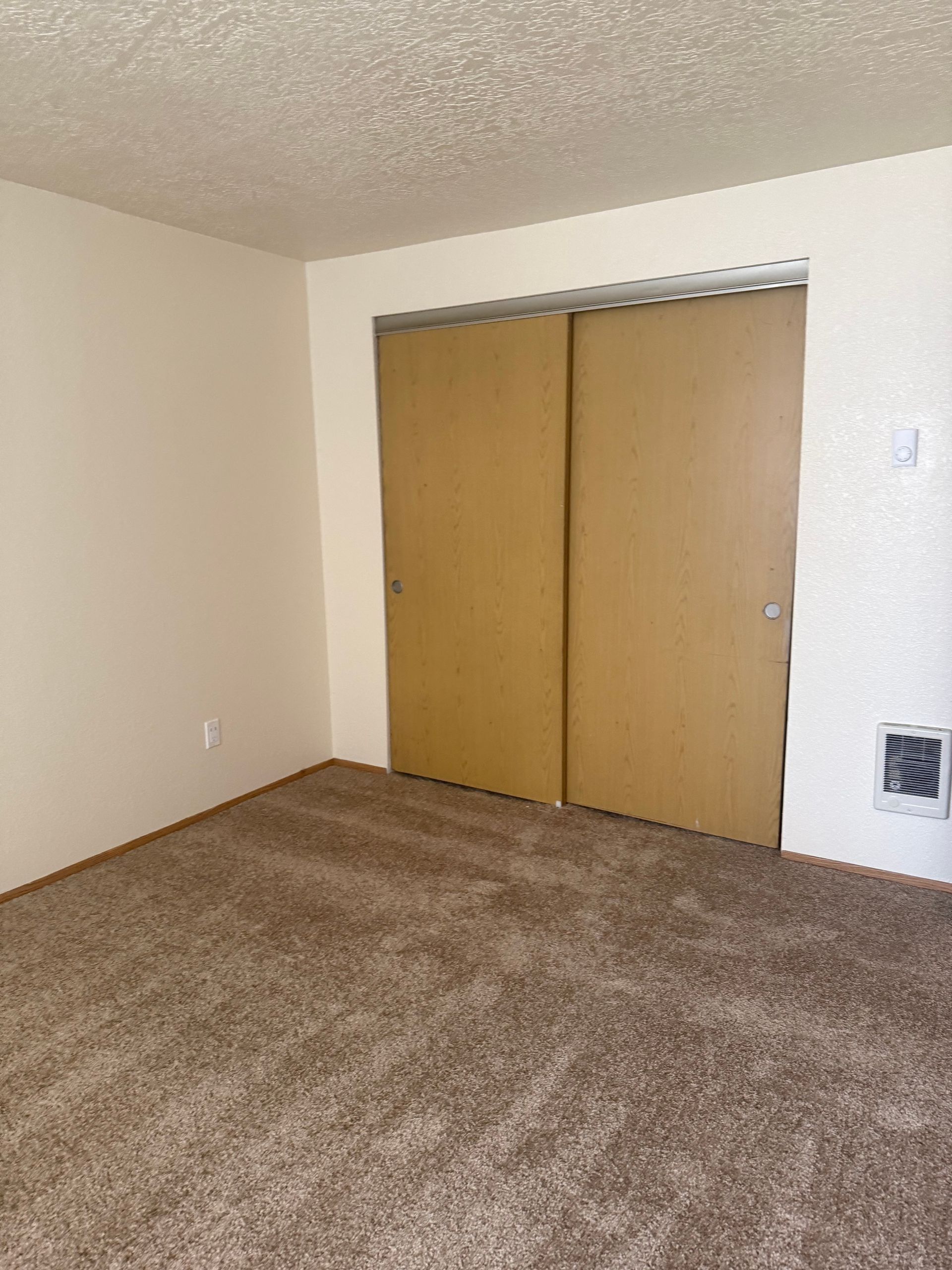 Empty carpeted bedroom with beige walls and sliding wooden closet doors.