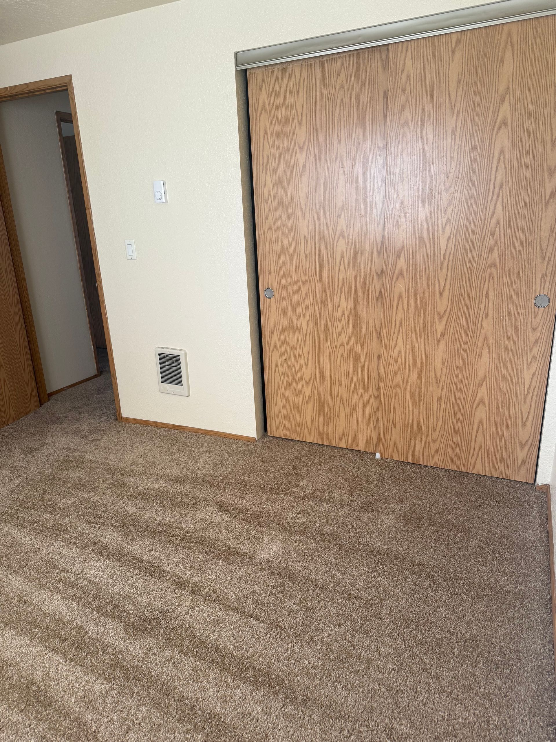 Empty carpeted room with beige walls and large wood sliding closet doors