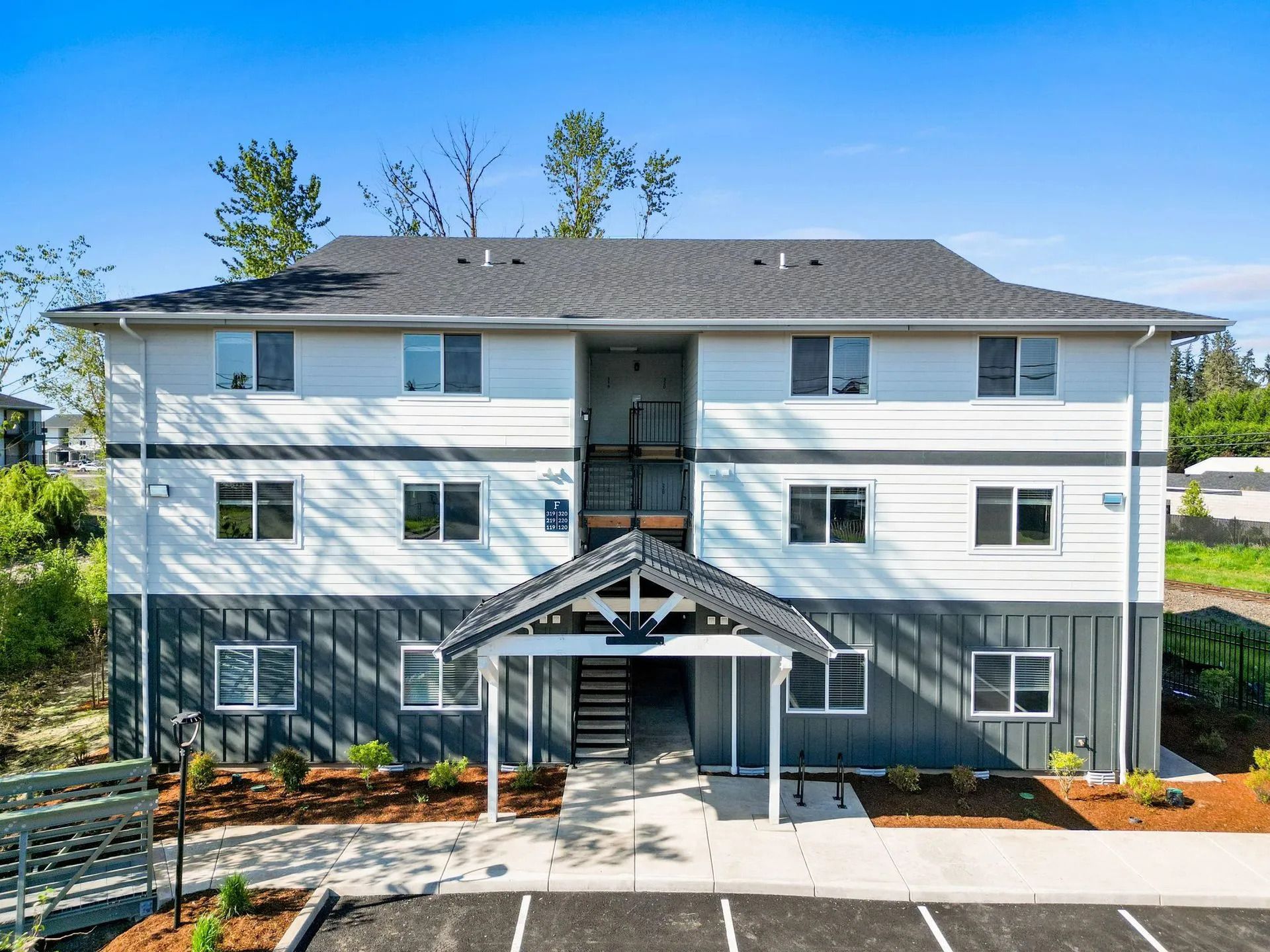 Modern three-story apartment building with gray siding and white trim, front entrance, and landscaped grounds