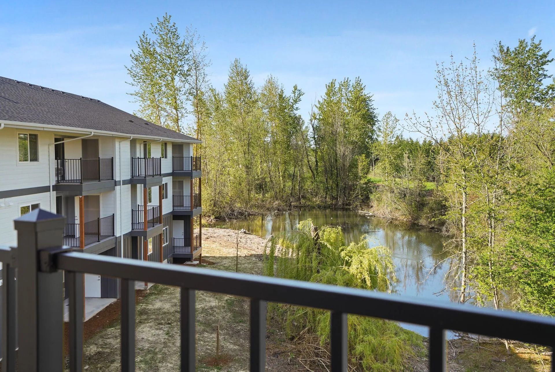 Balcony view of an apartment complex beside a calm river and trees on a sunny day