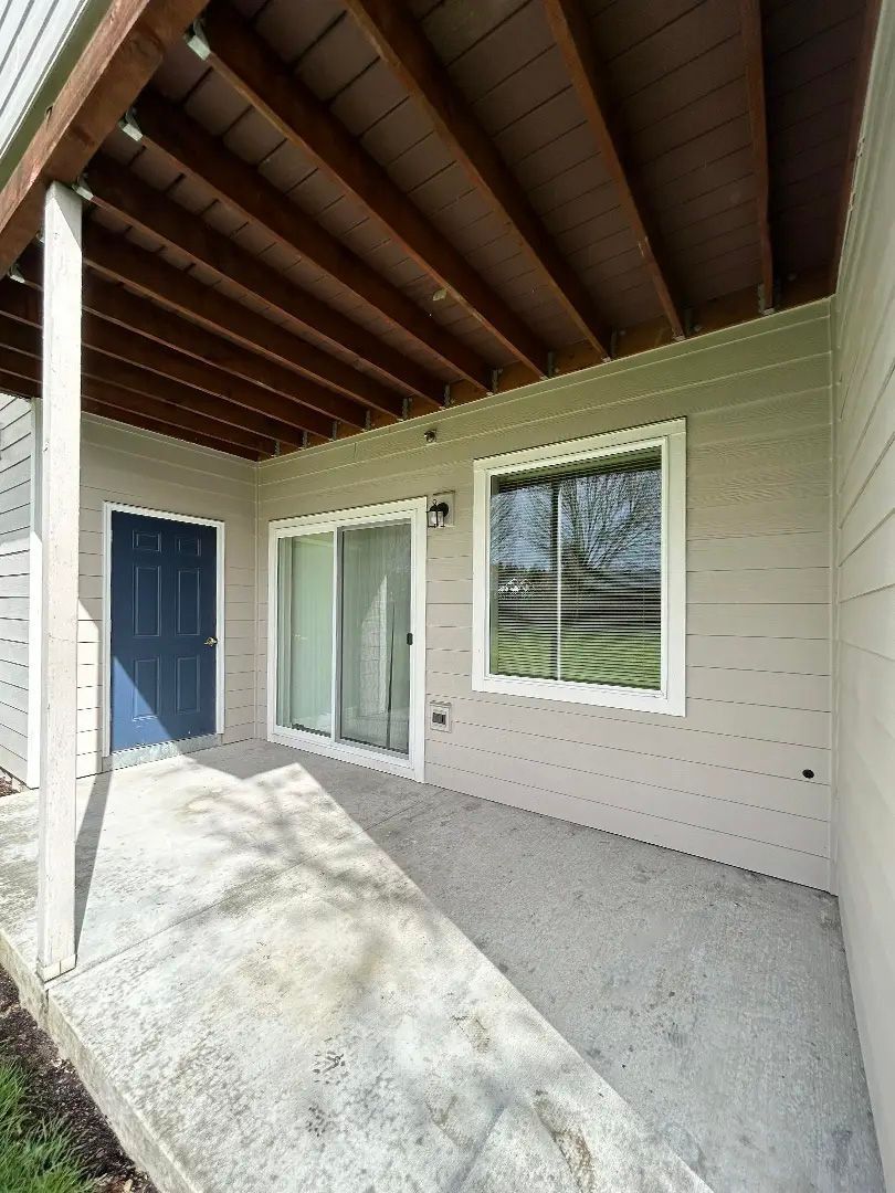 Covered patio with exposed wood ceiling, blue door, sliding glass door, and window on a beige house.