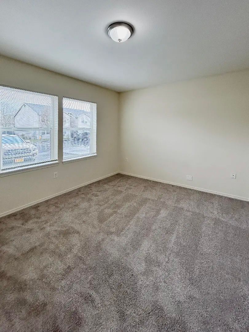 Empty beige bedroom with carpet, window blinds, and a ceiling light