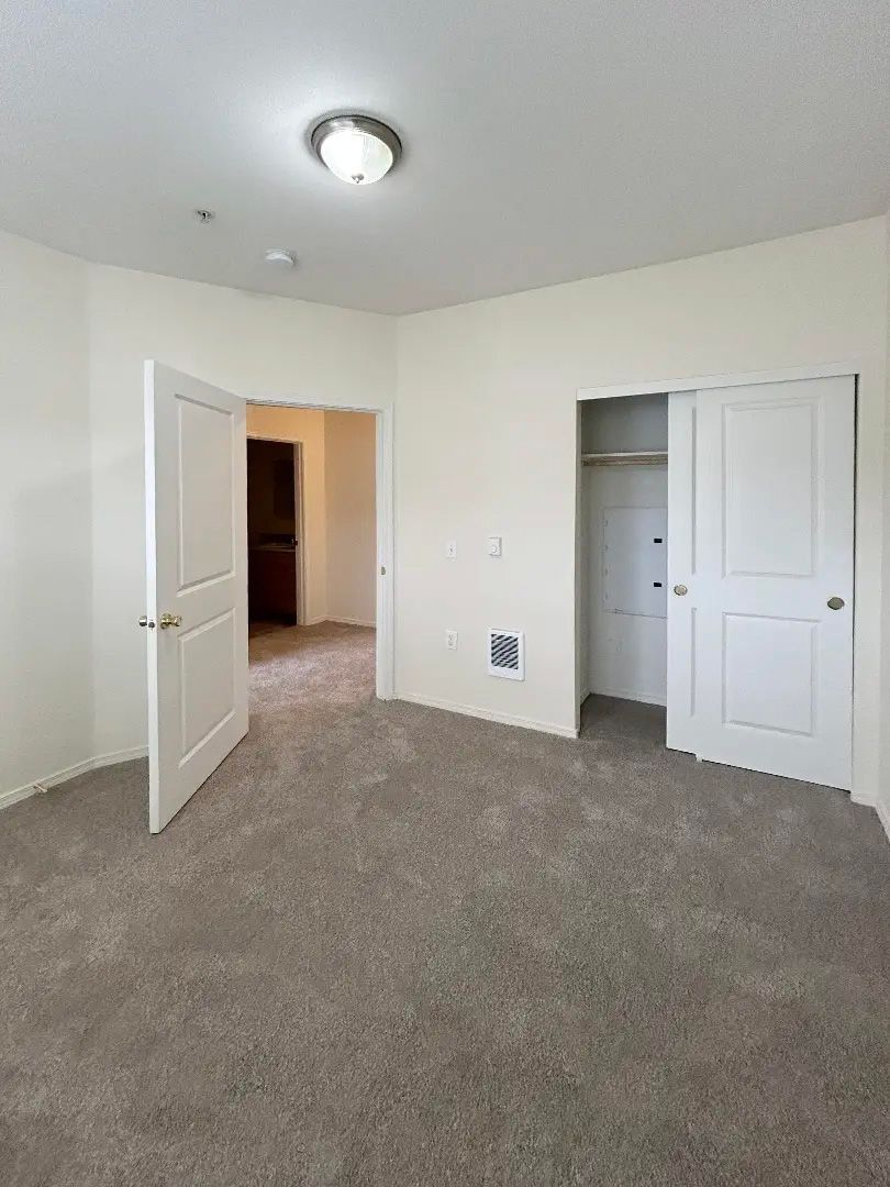 Empty beige bedroom with open closet doors and carpeted floor